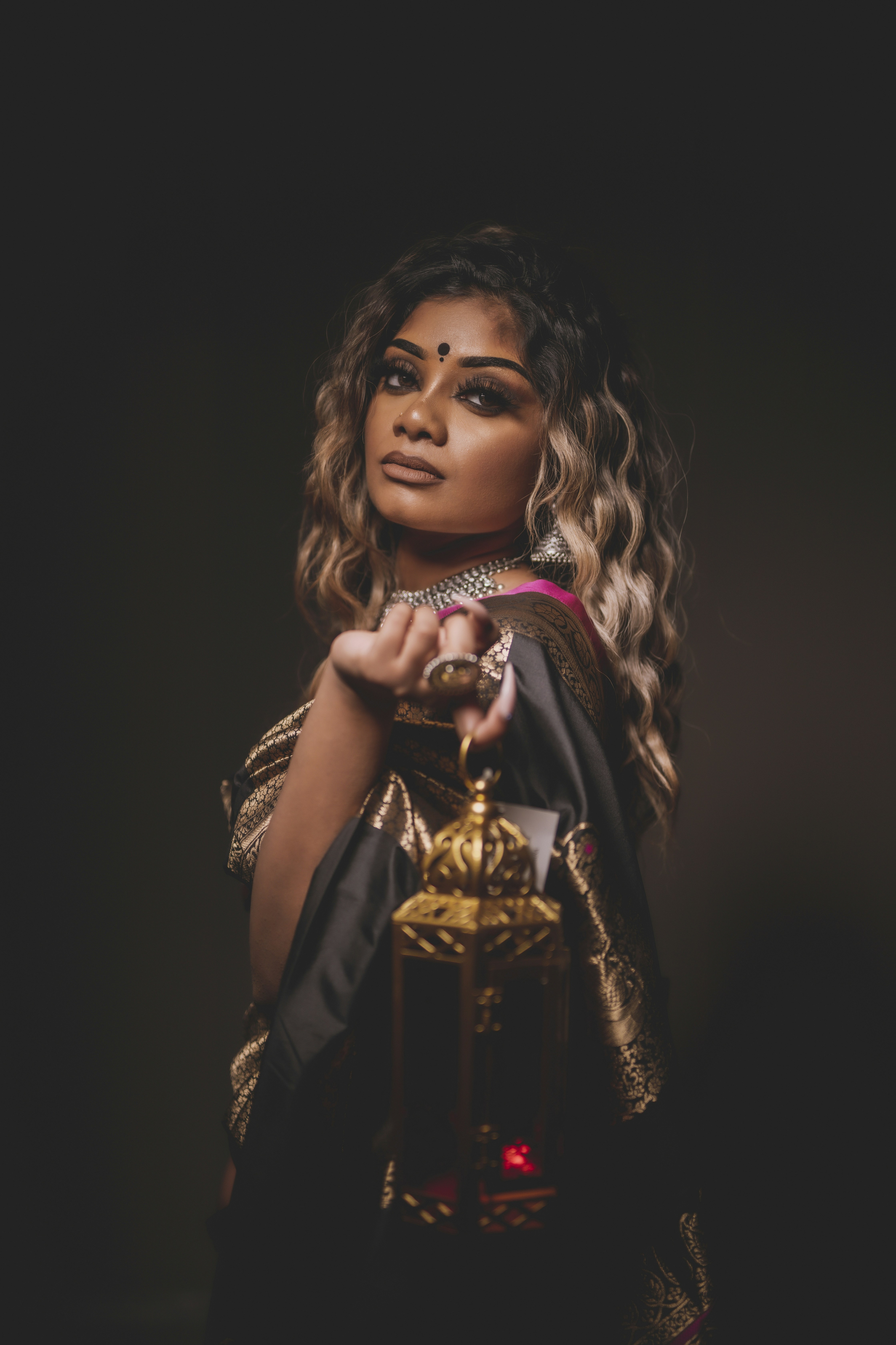 A woman in a black and gold sari holding a decorative metal lantern