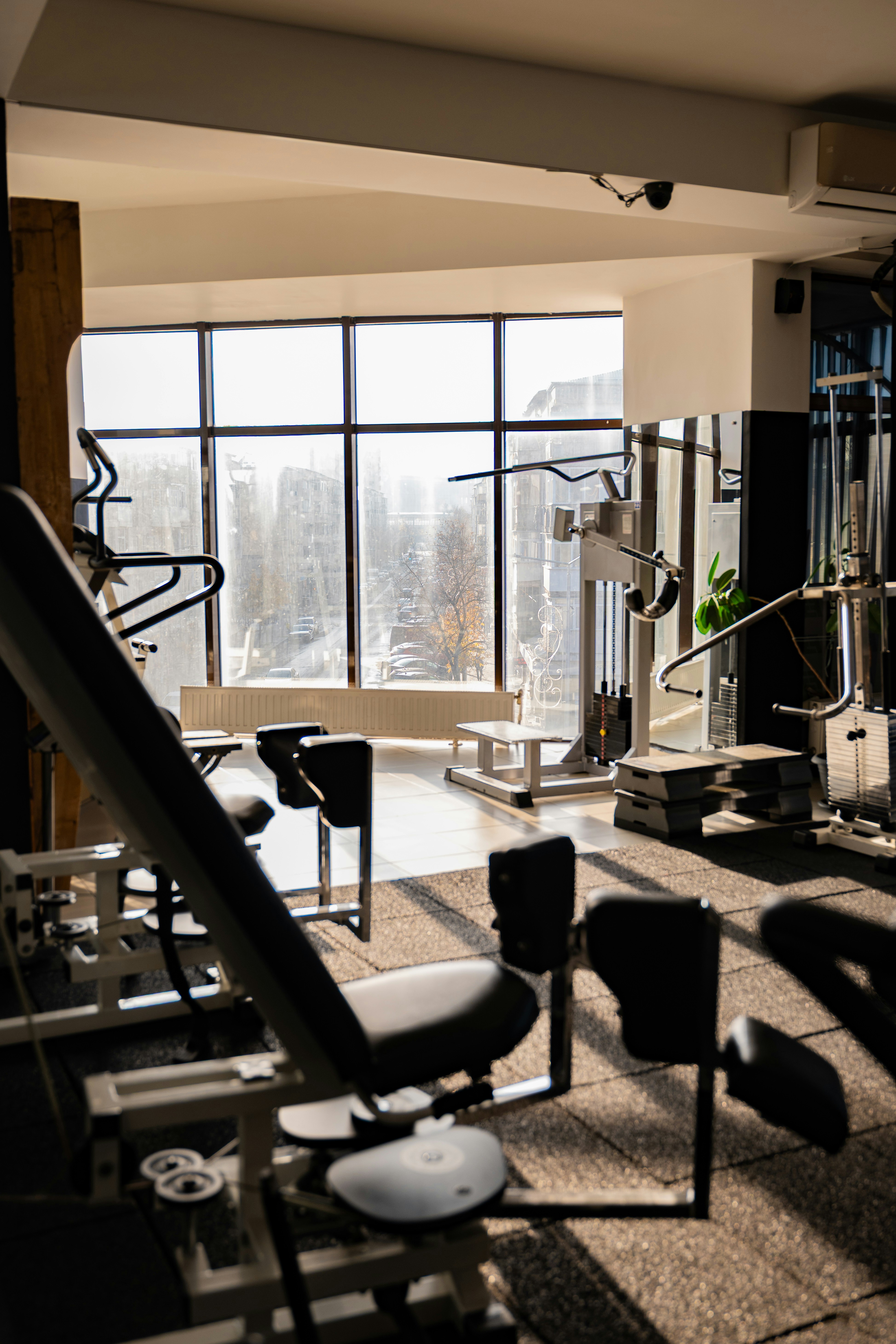 Weight machines and benches in a sunlit gym with large windows