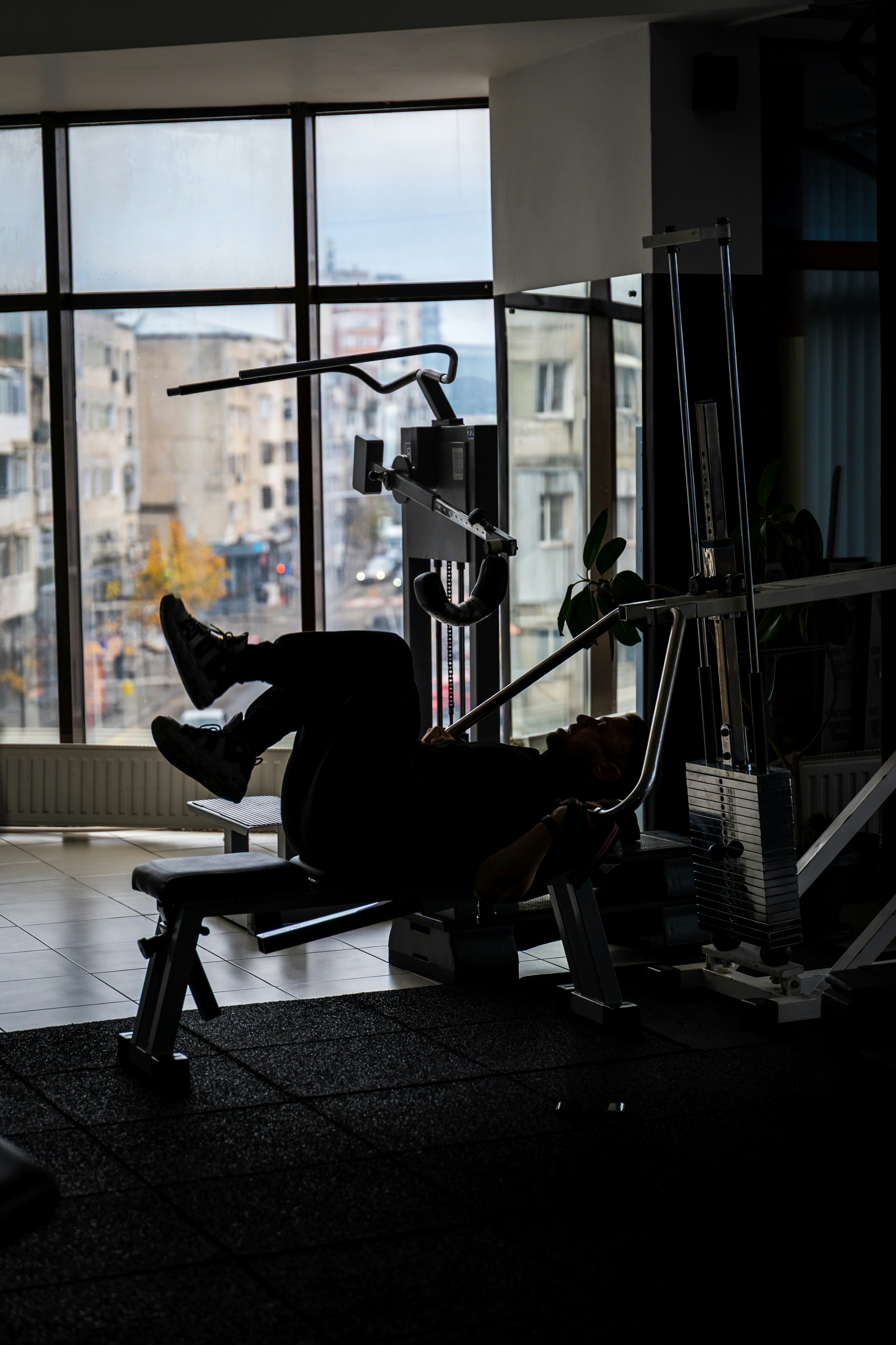 A person in silhouette exercising on a gym bench before a large window