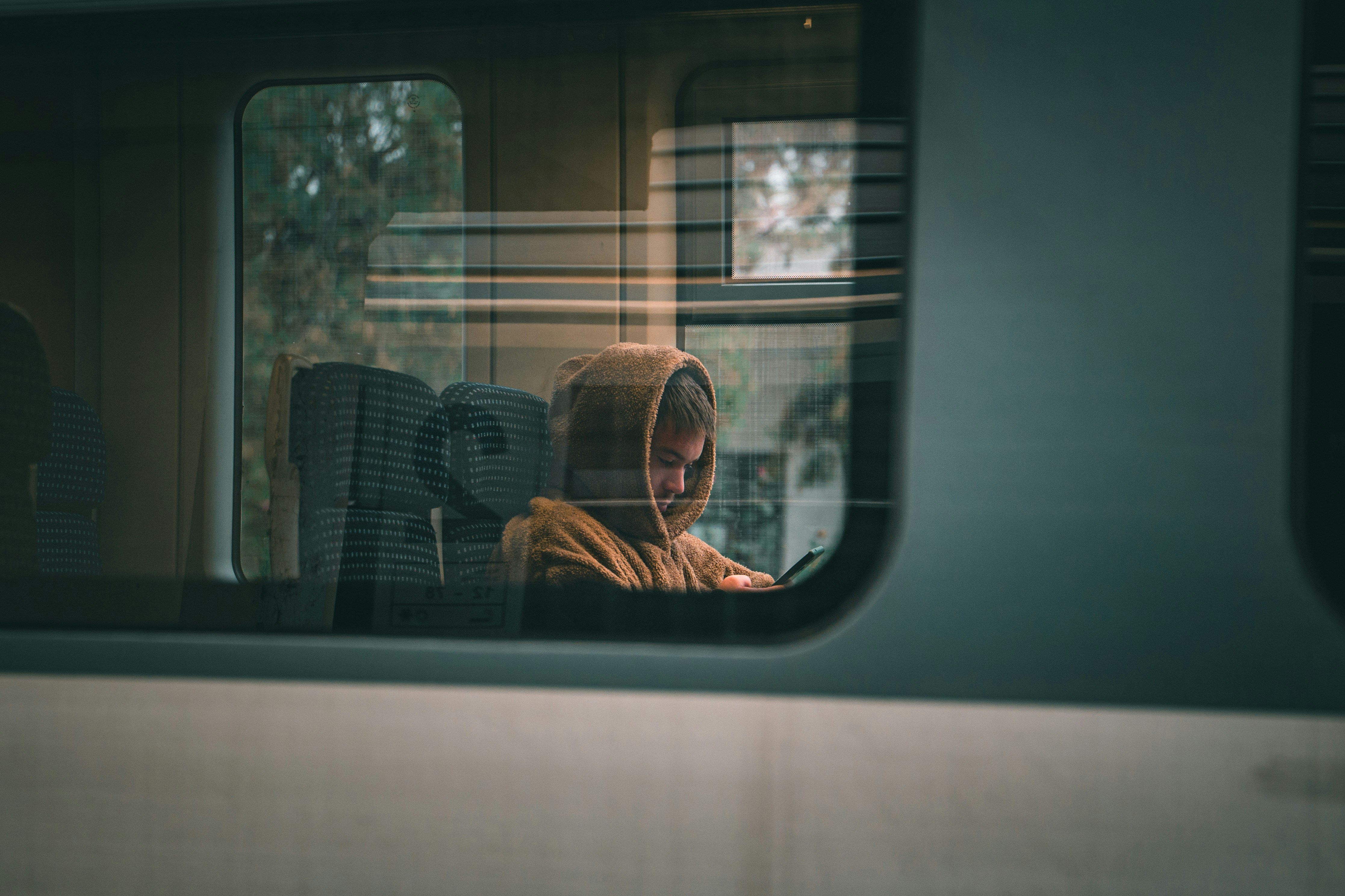 Person in a brown hoodie seen through a train window