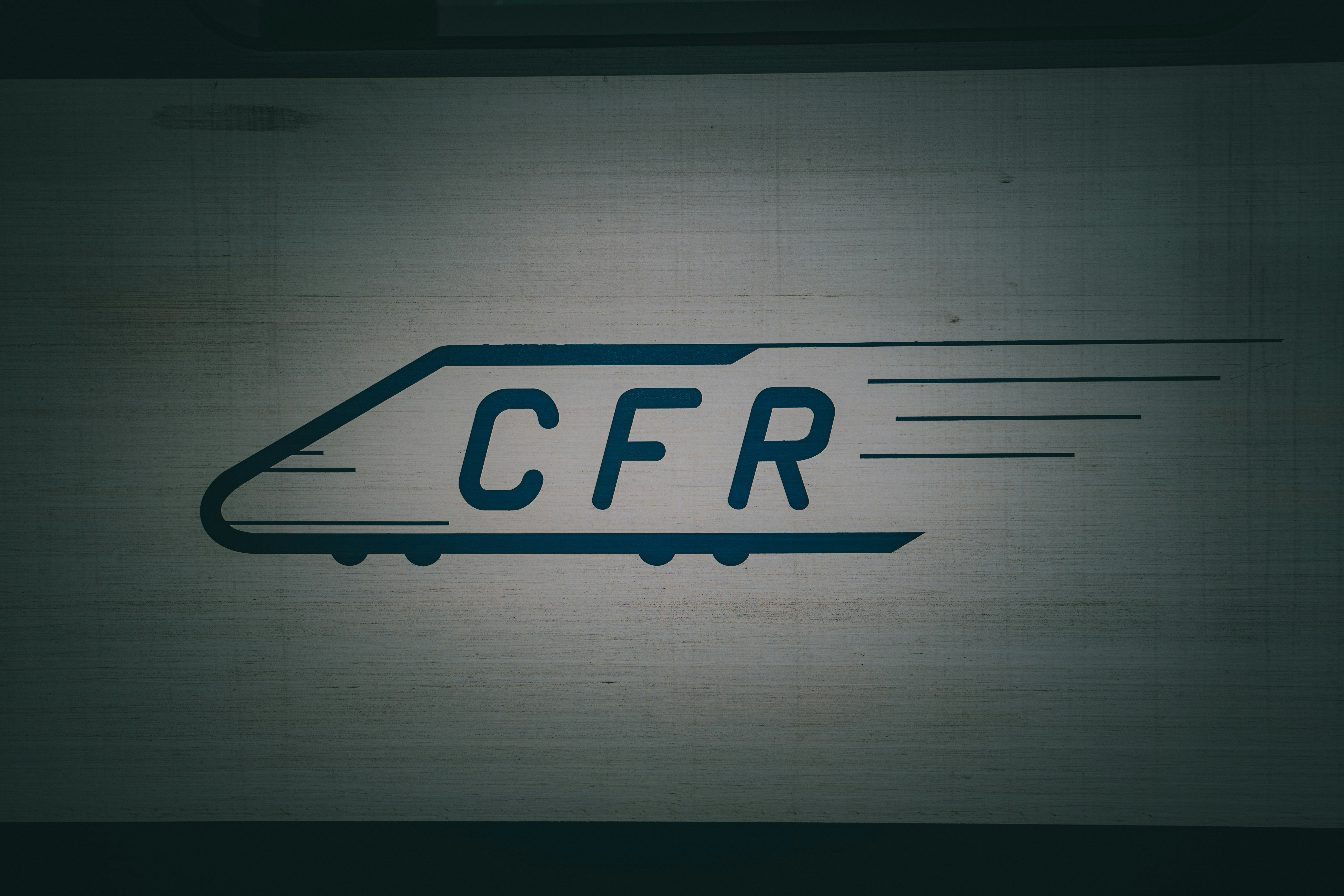 A dark blue train logo with the letters CFR on a light grey surface