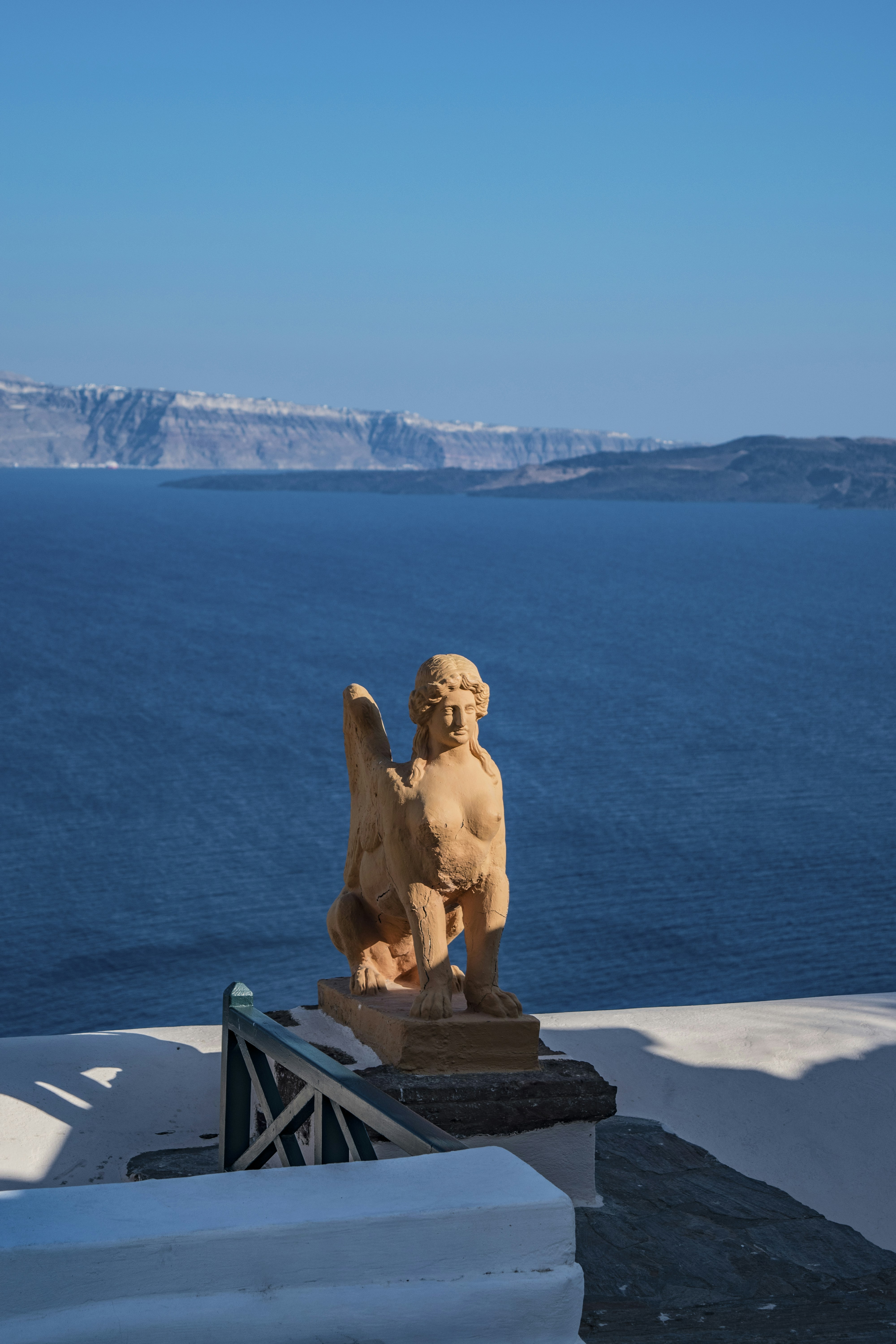 A stone sphinx statue overlooking the blue Aegean Sea in Santorini, Greece