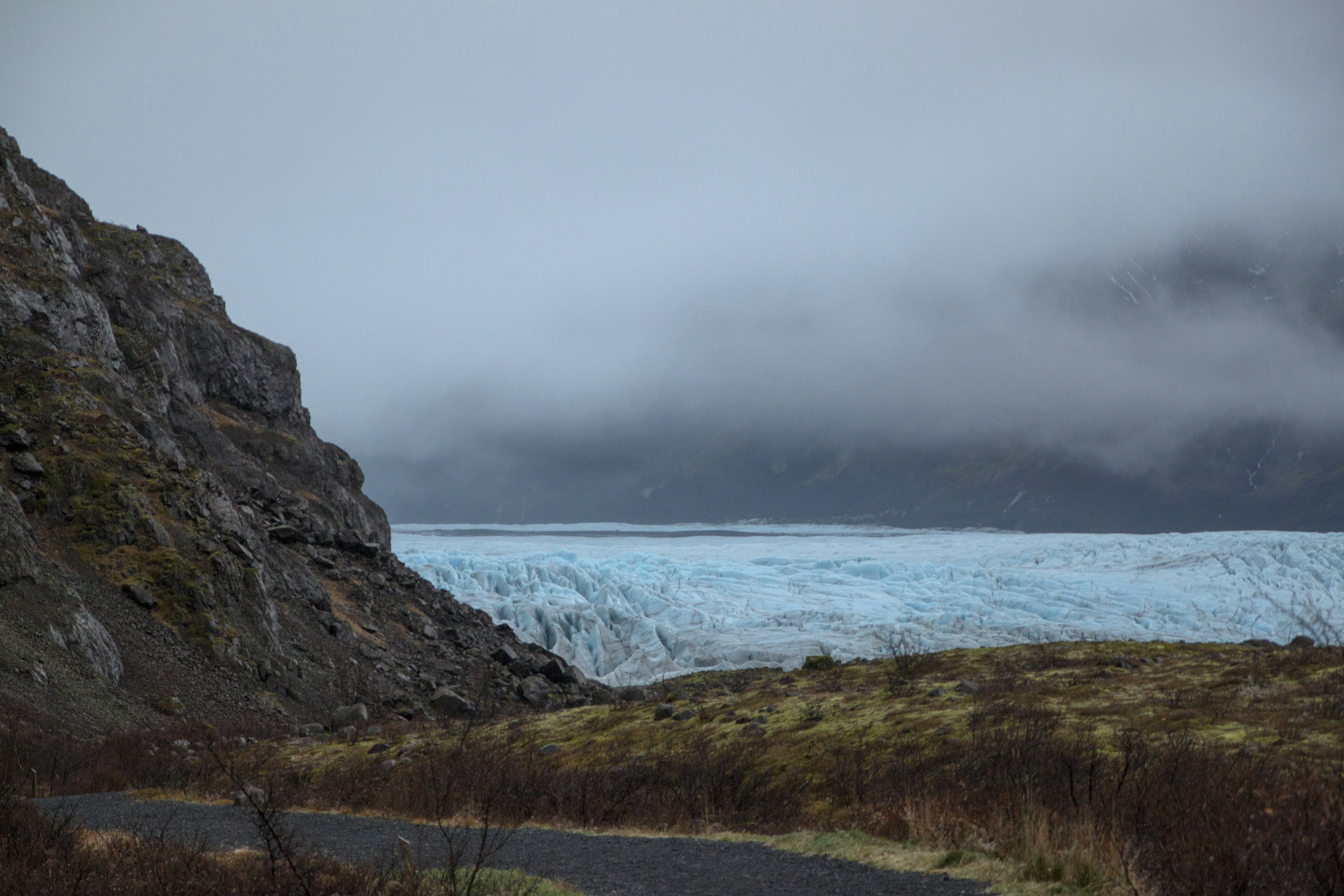 A blue glacier tongue between rocky slopes under a heavy blanket of fog