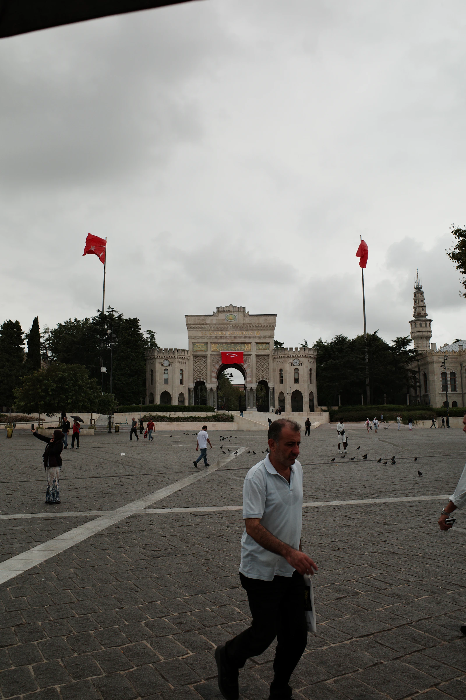 People walking across a stone plaza toward the ornate gate of Istanbul University