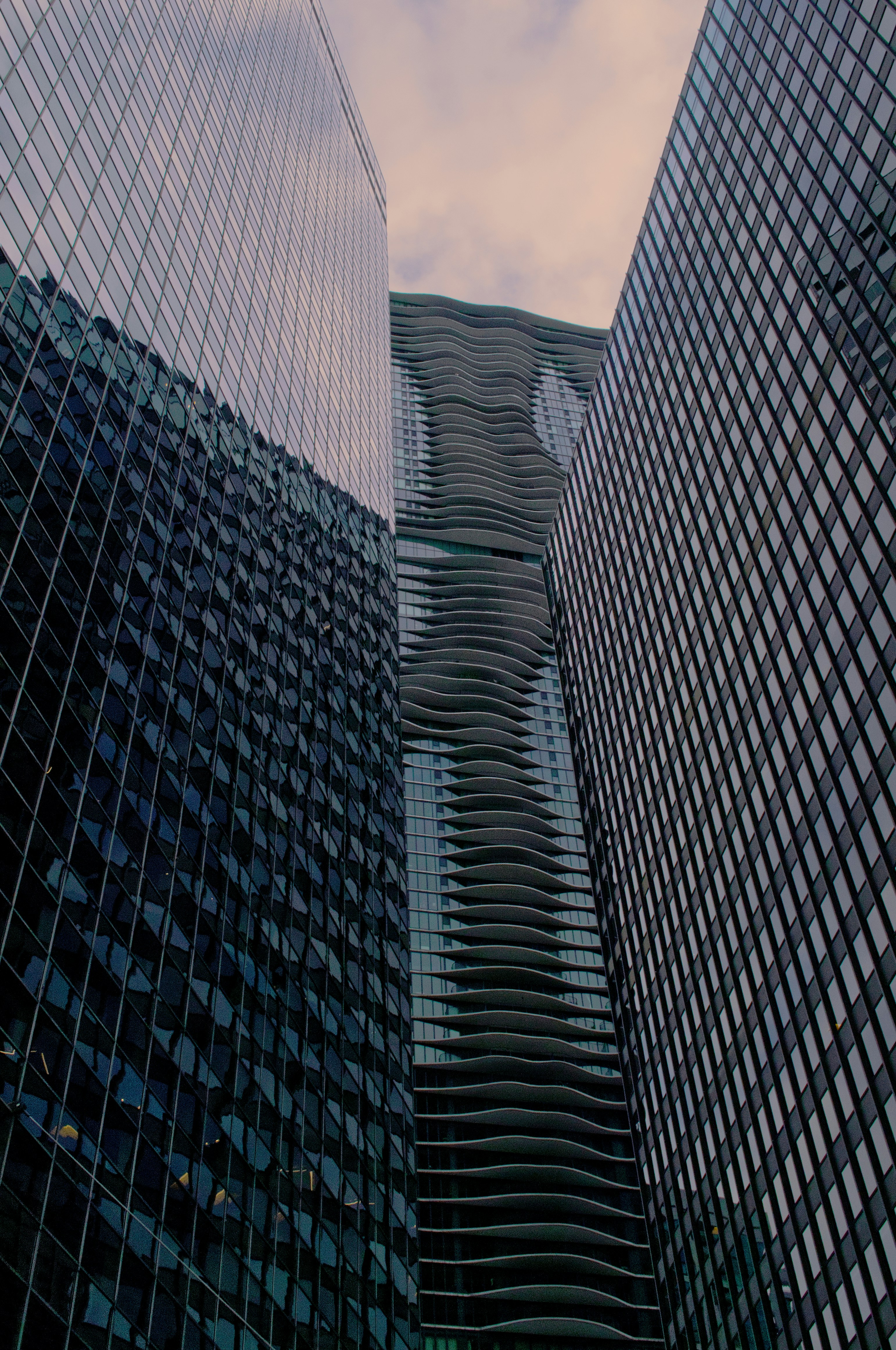 A wavy skyscraper between two glass office buildings under a cloudy sky