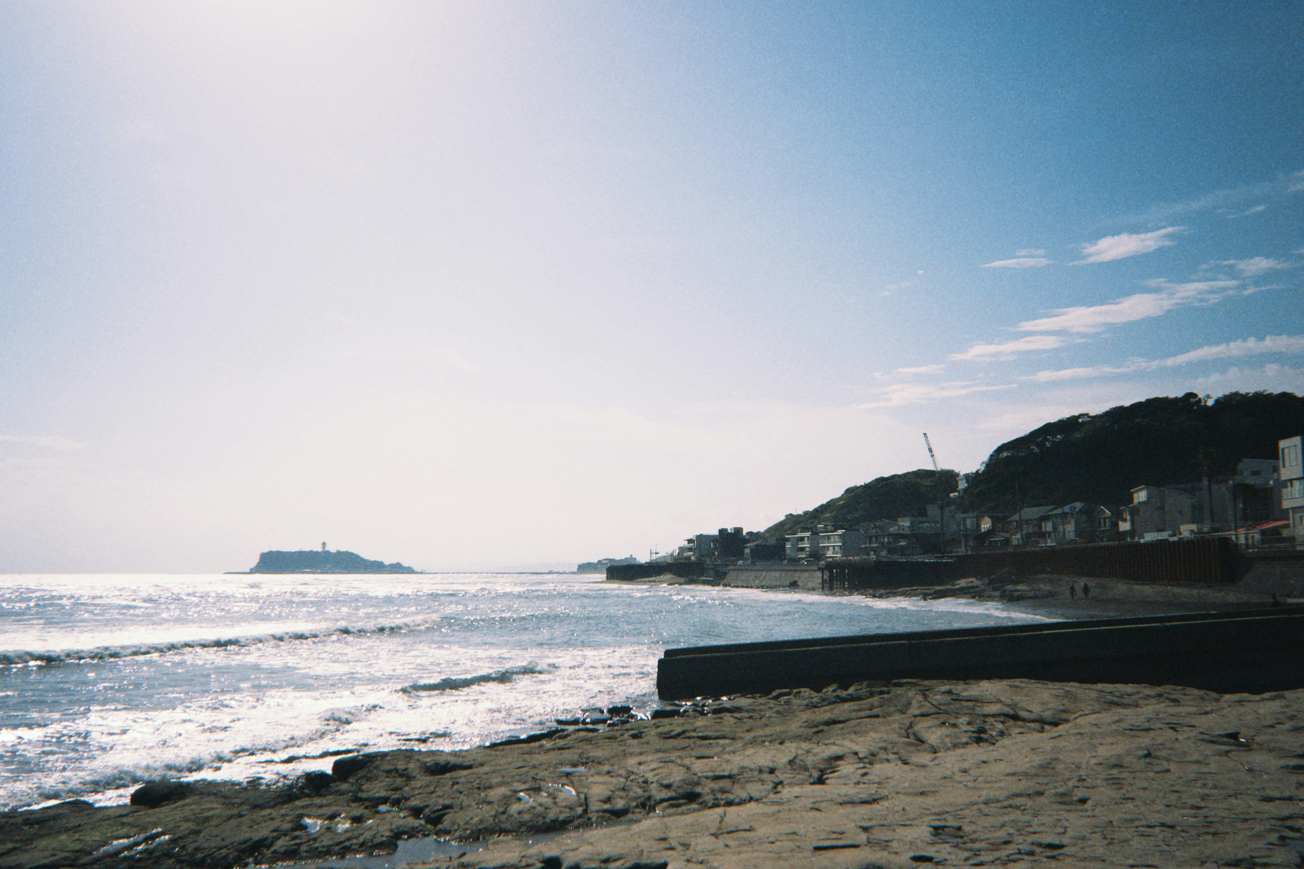 A rocky coastline with a distant island and buildings along the shore
