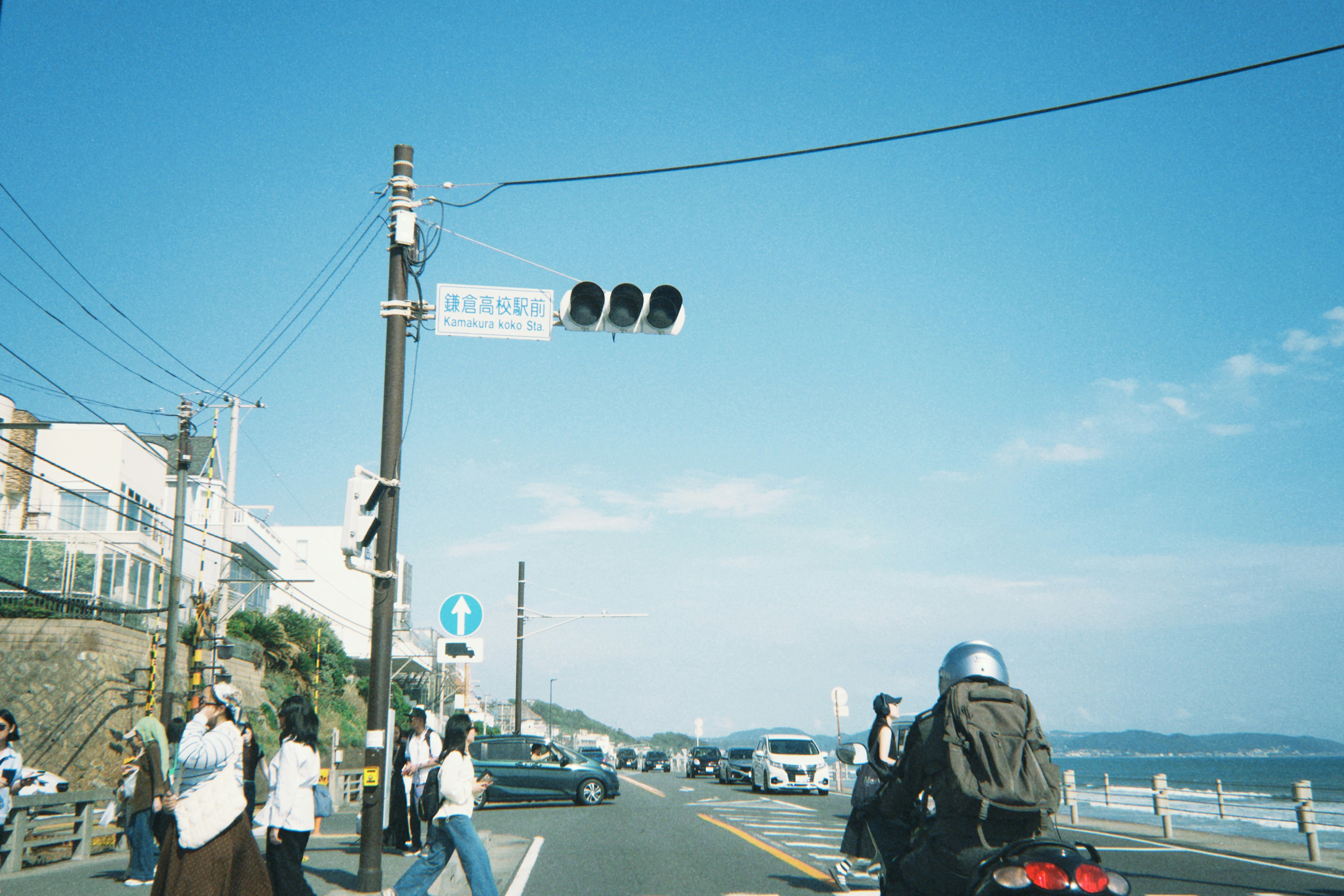People walking along a coastal road near Kamakura Koko-mae Station in Japan