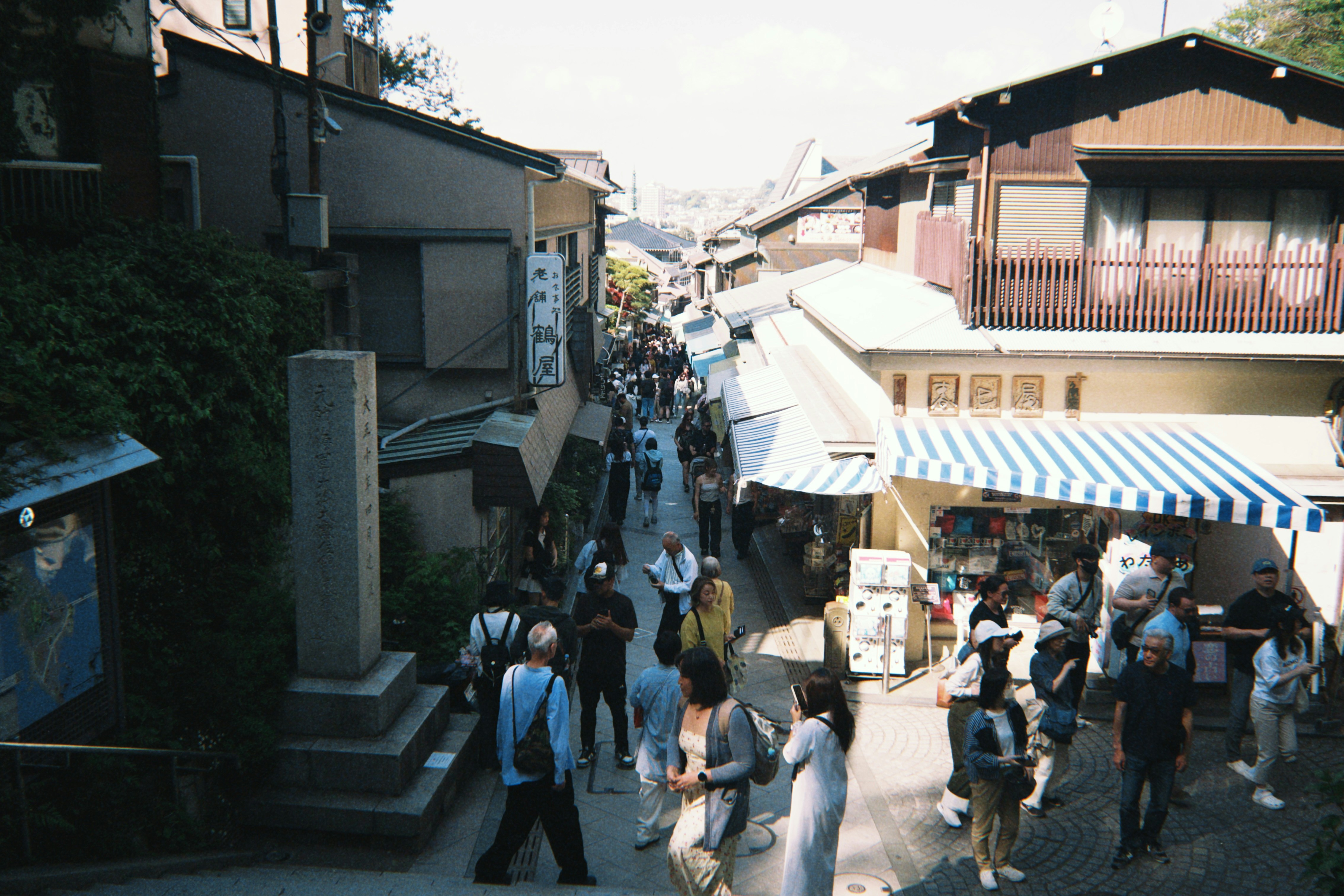 A narrow street in Kamakura lined with traditional buildings and shops filled with people