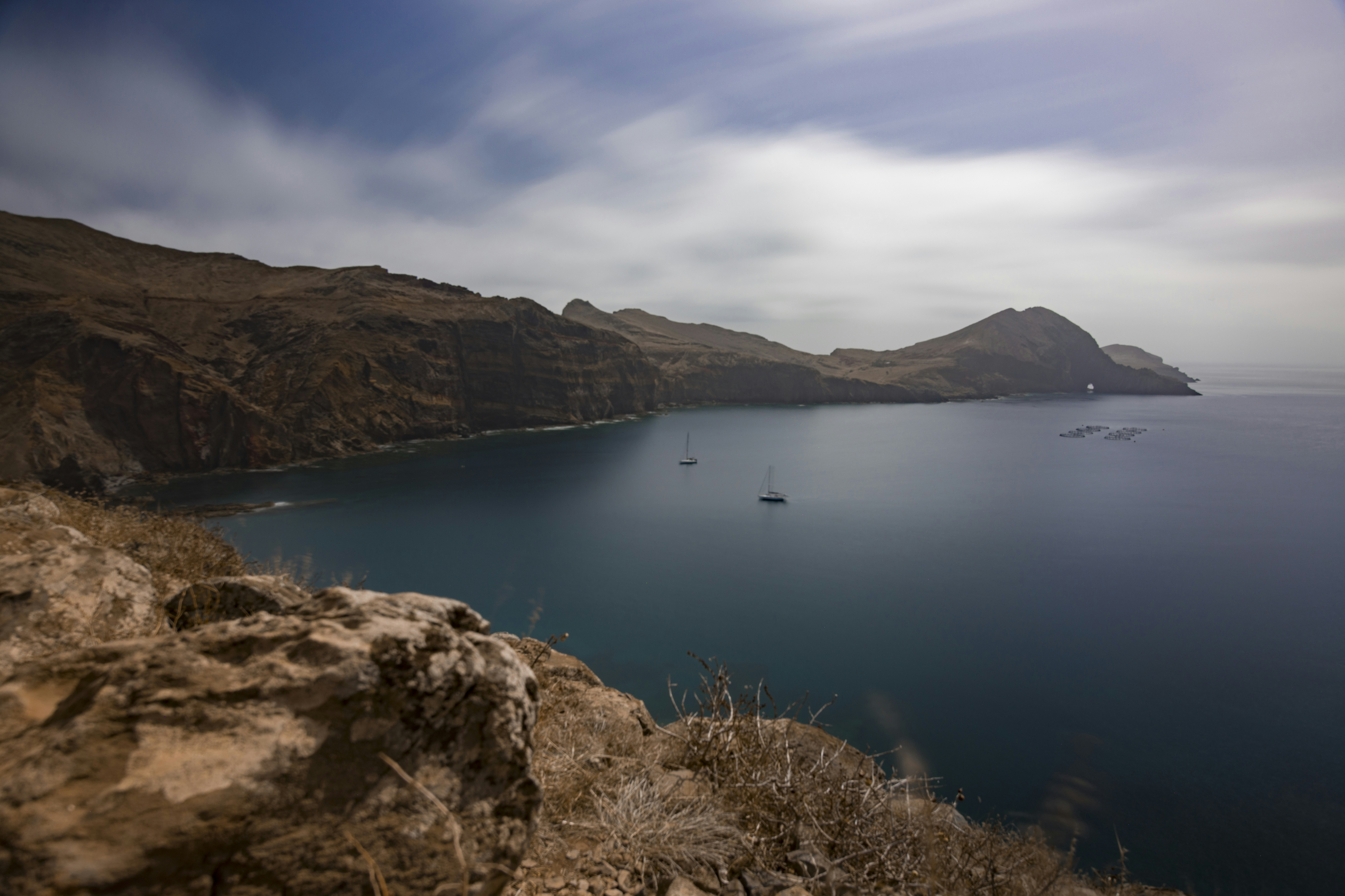 Two sailboats on calm water in a bay surrounded by rocky cliffs