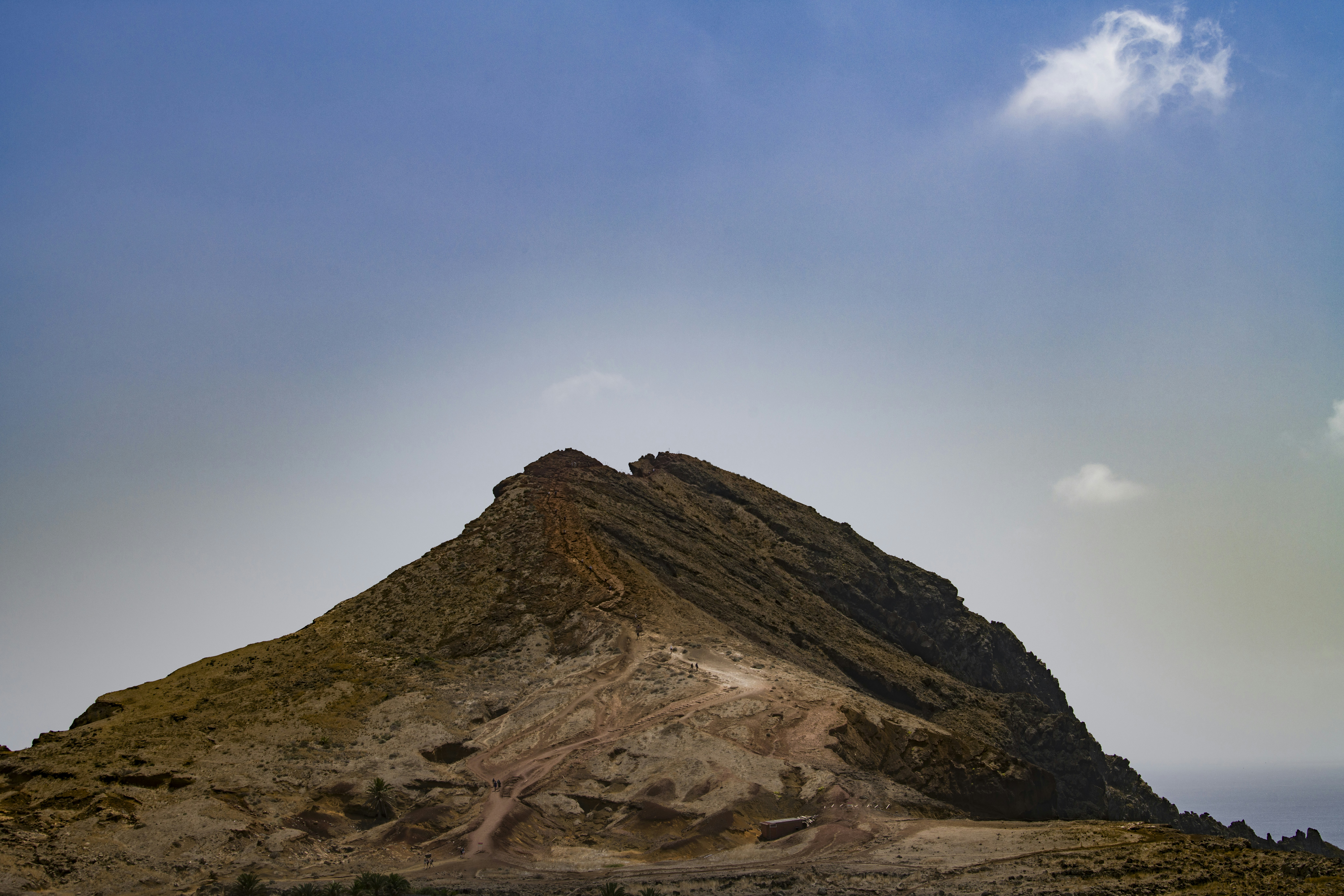 A rocky mountain peak with a dirt path under a clear blue sky