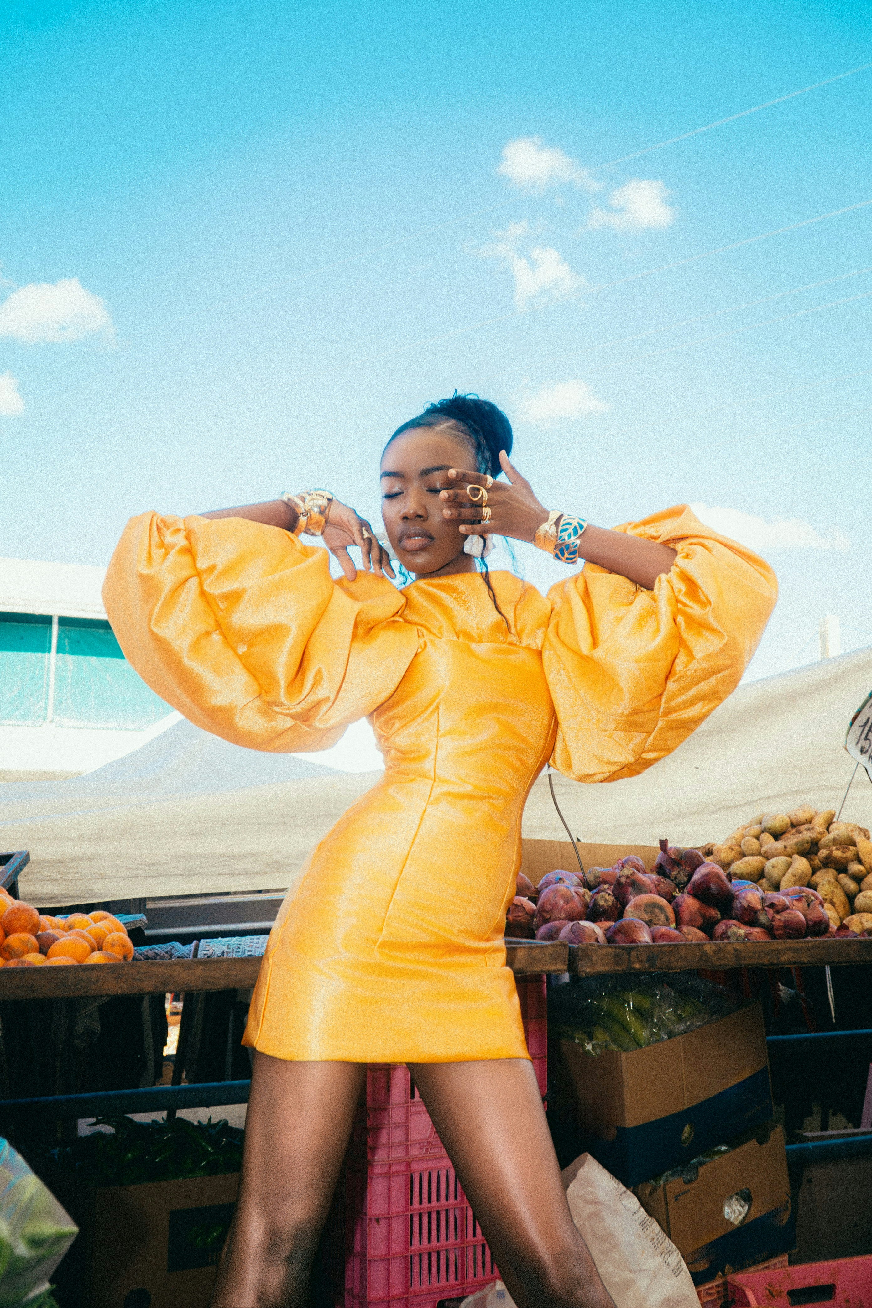 A woman in a bright yellow dress posing at an outdoor produce market