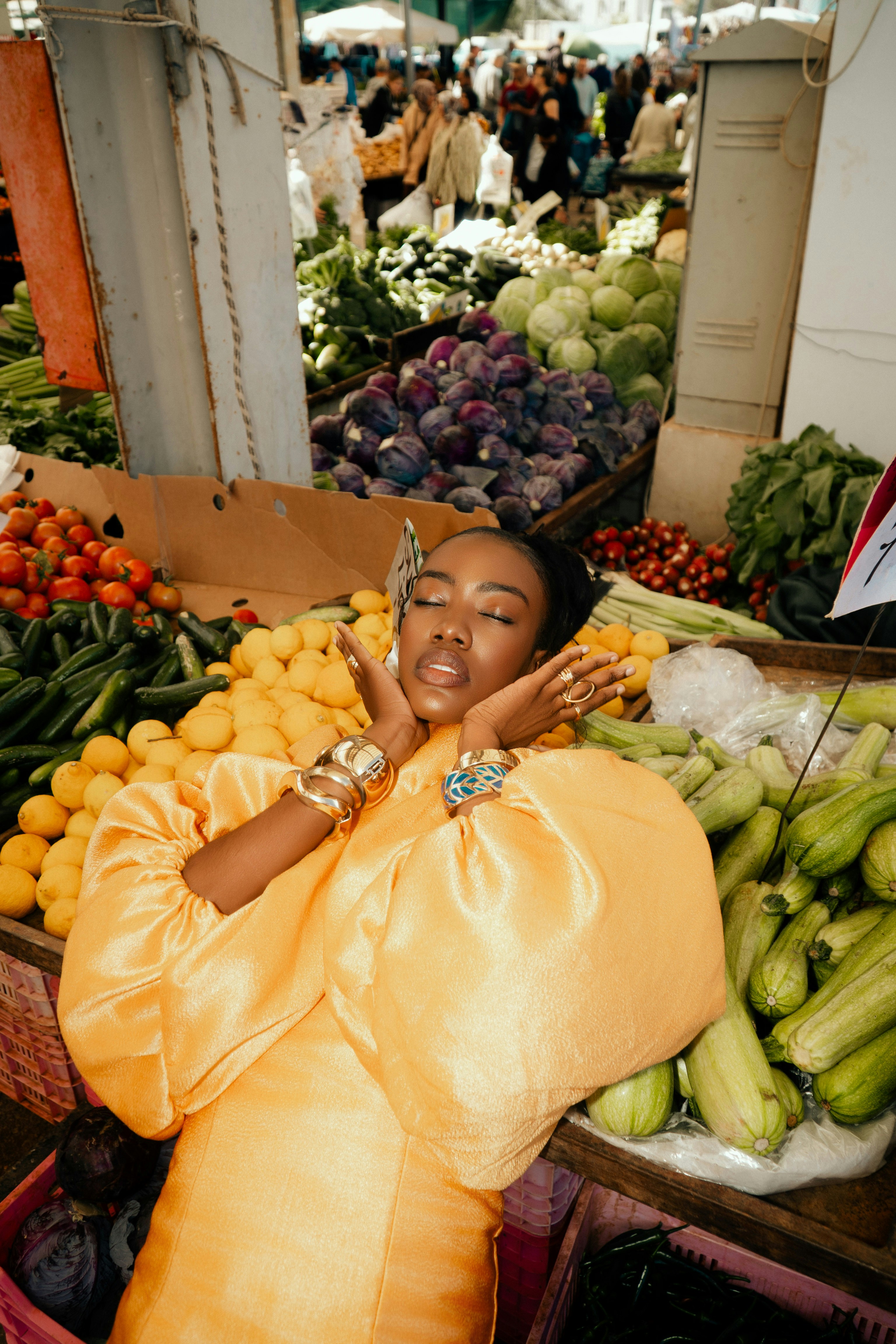 A woman in a yellow dress posing among fresh produce at a market
