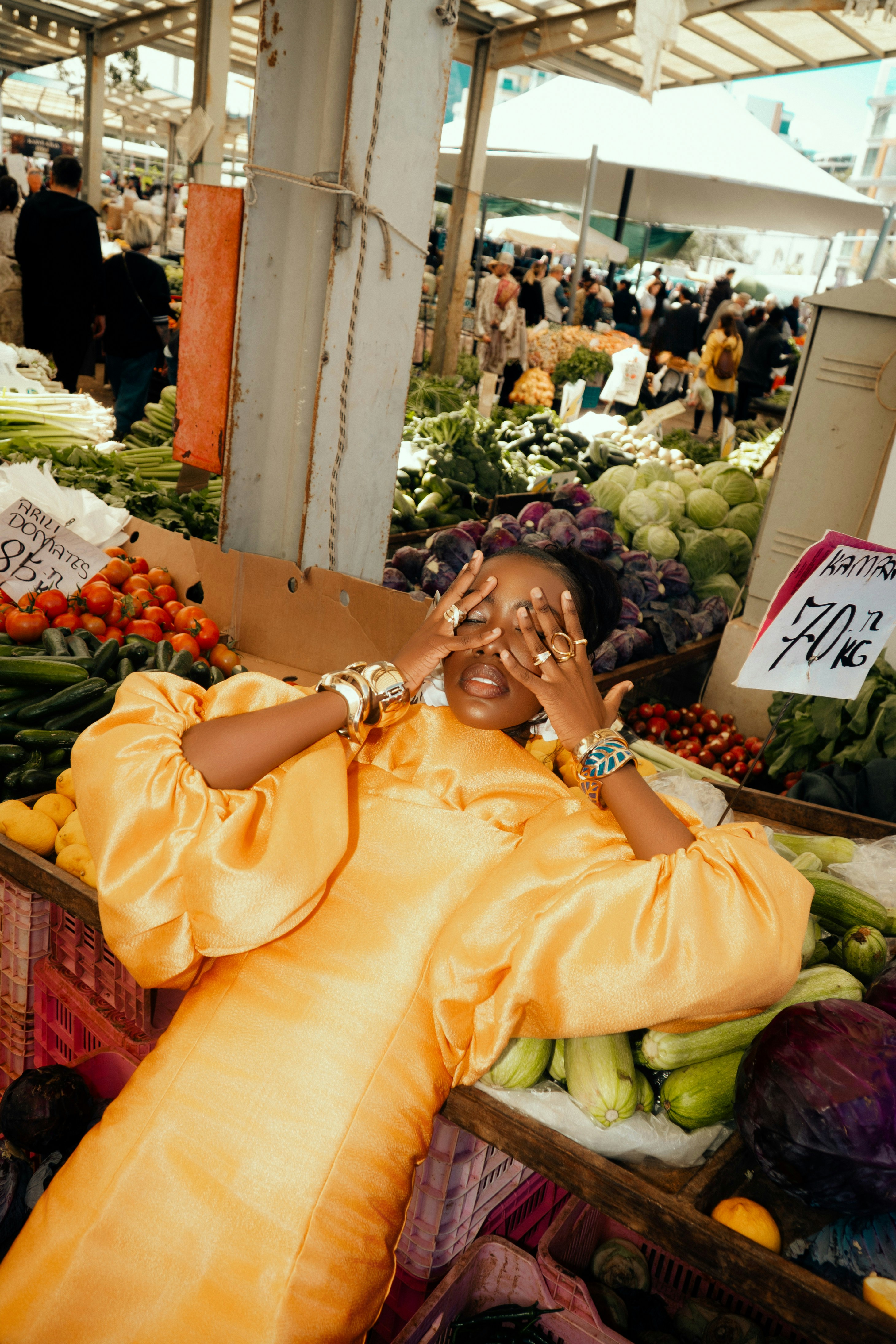 A woman in a yellow dress posing among fresh vegetables at an outdoor market