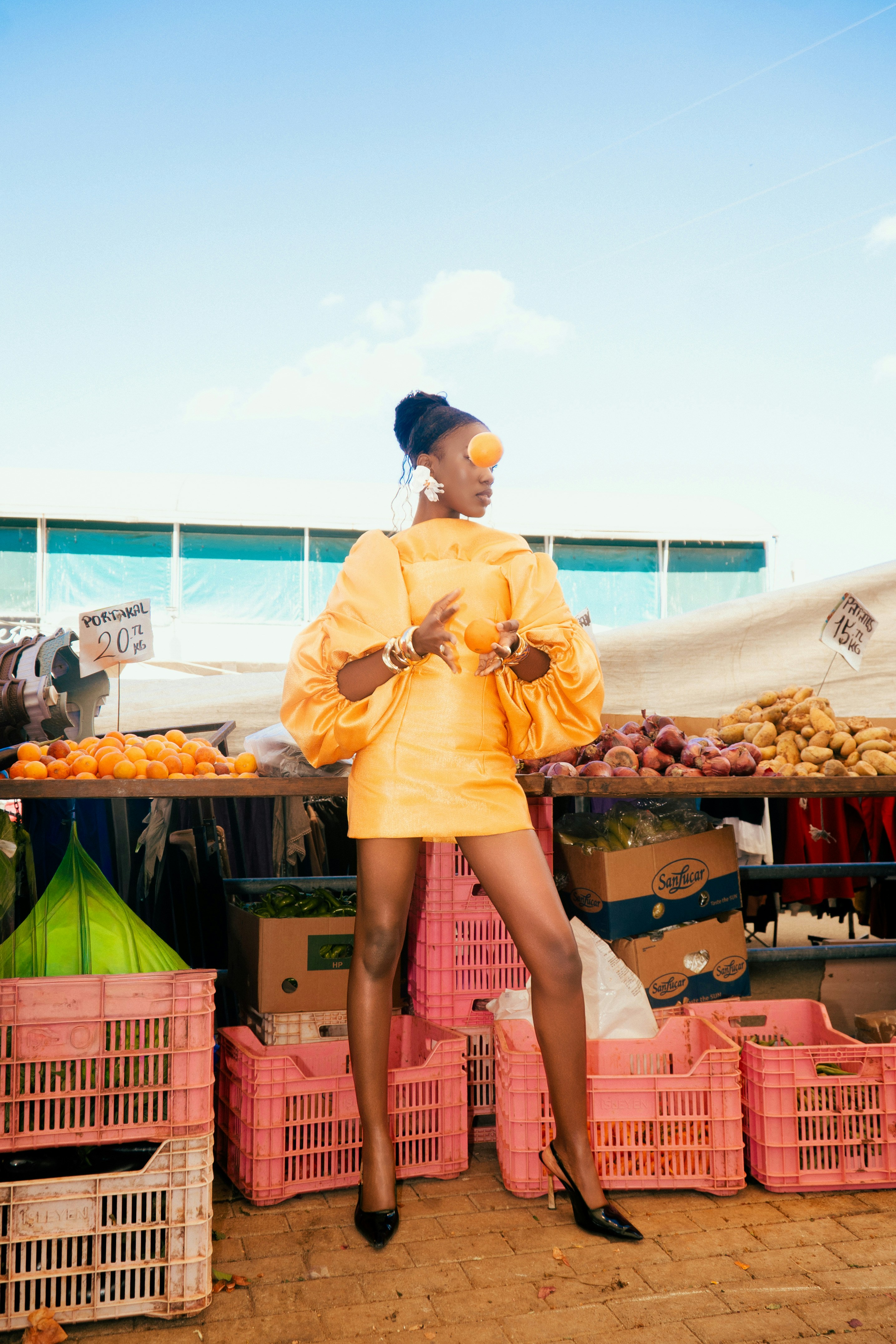 A woman in a yellow dress holding oranges at a market stall