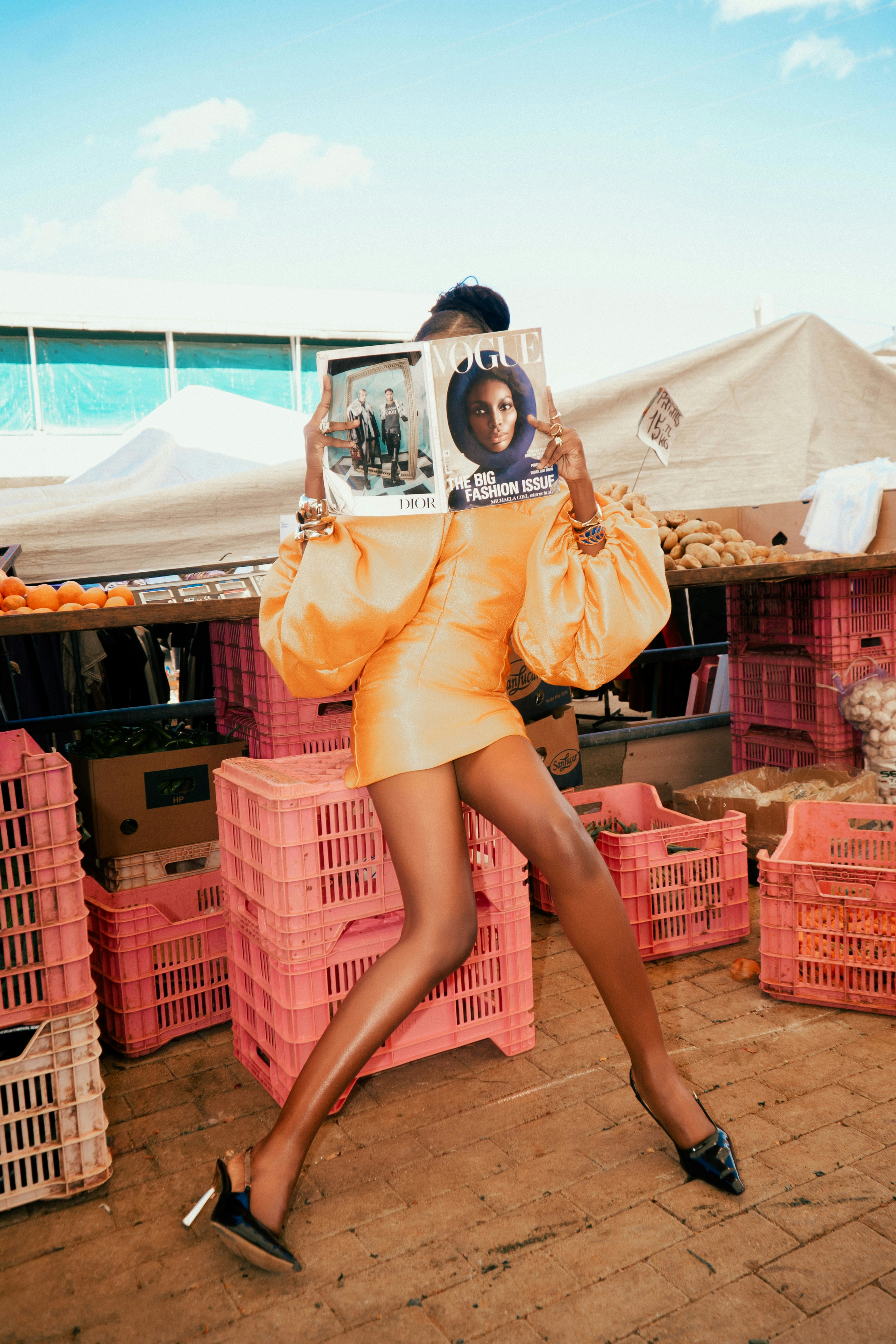A person in a yellow dress holding a Vogue magazine in a market