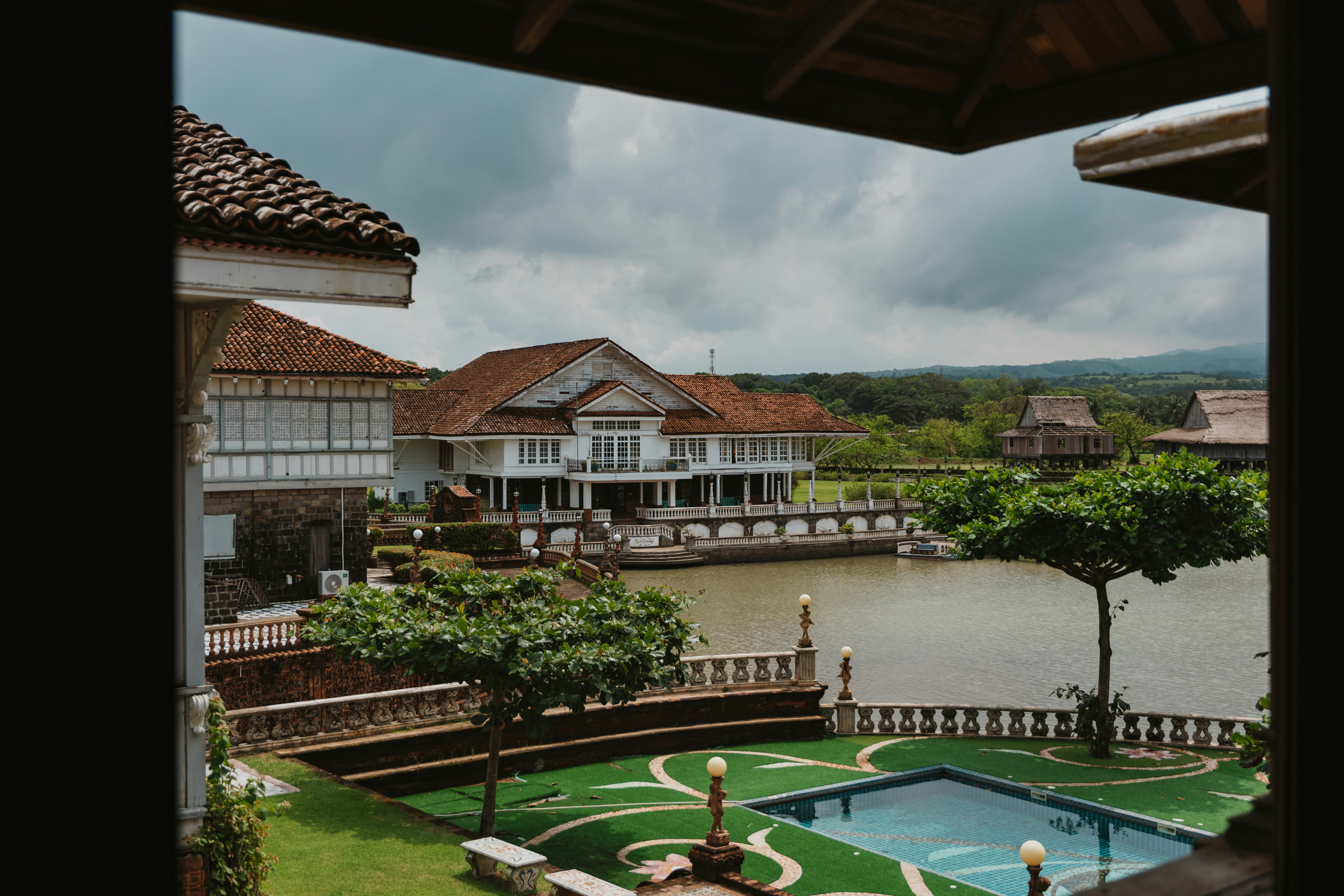 A colonial style mansion with a tiled roof overlooking a river and pool