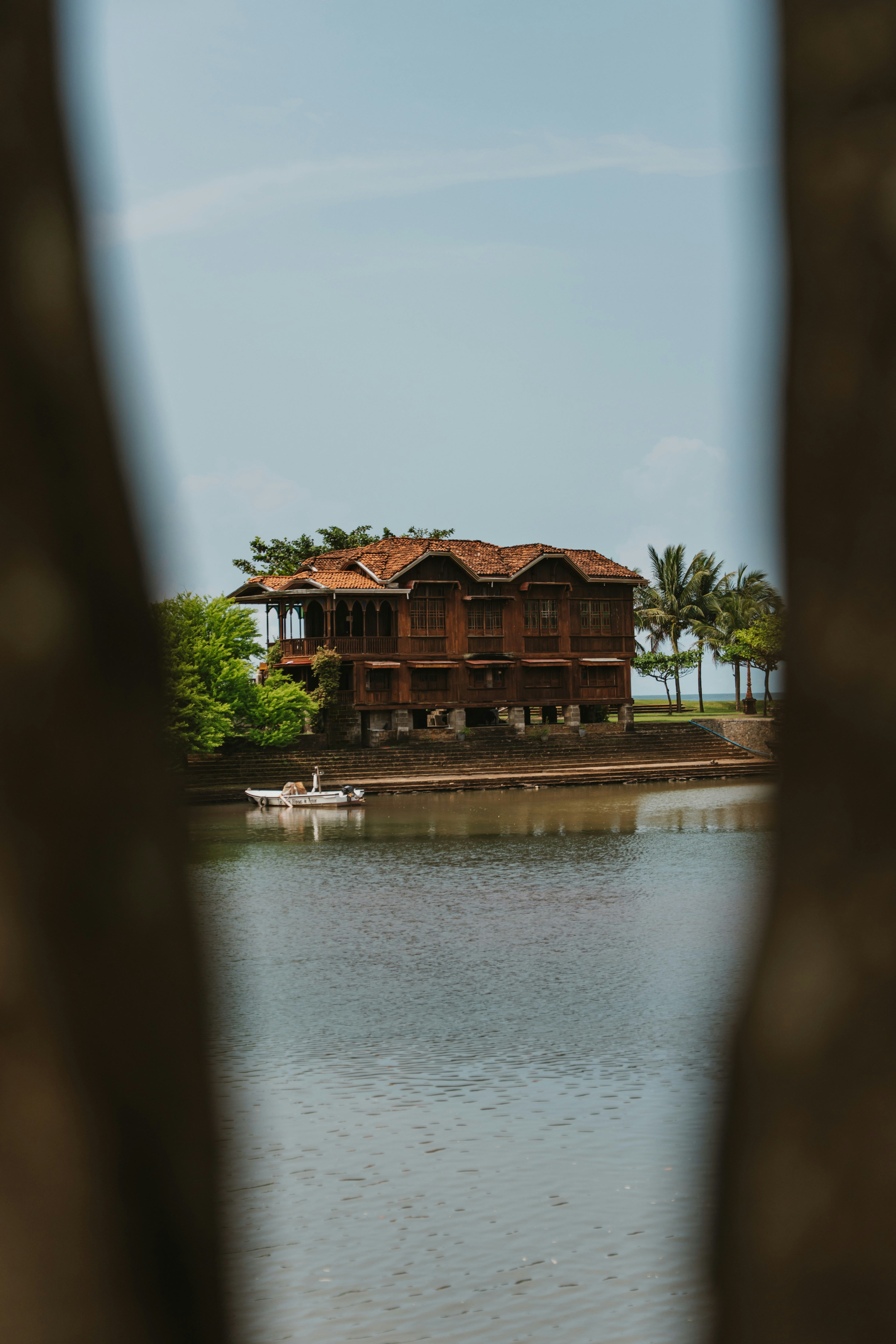 A wooden house on stilts by a calm river with a small boat