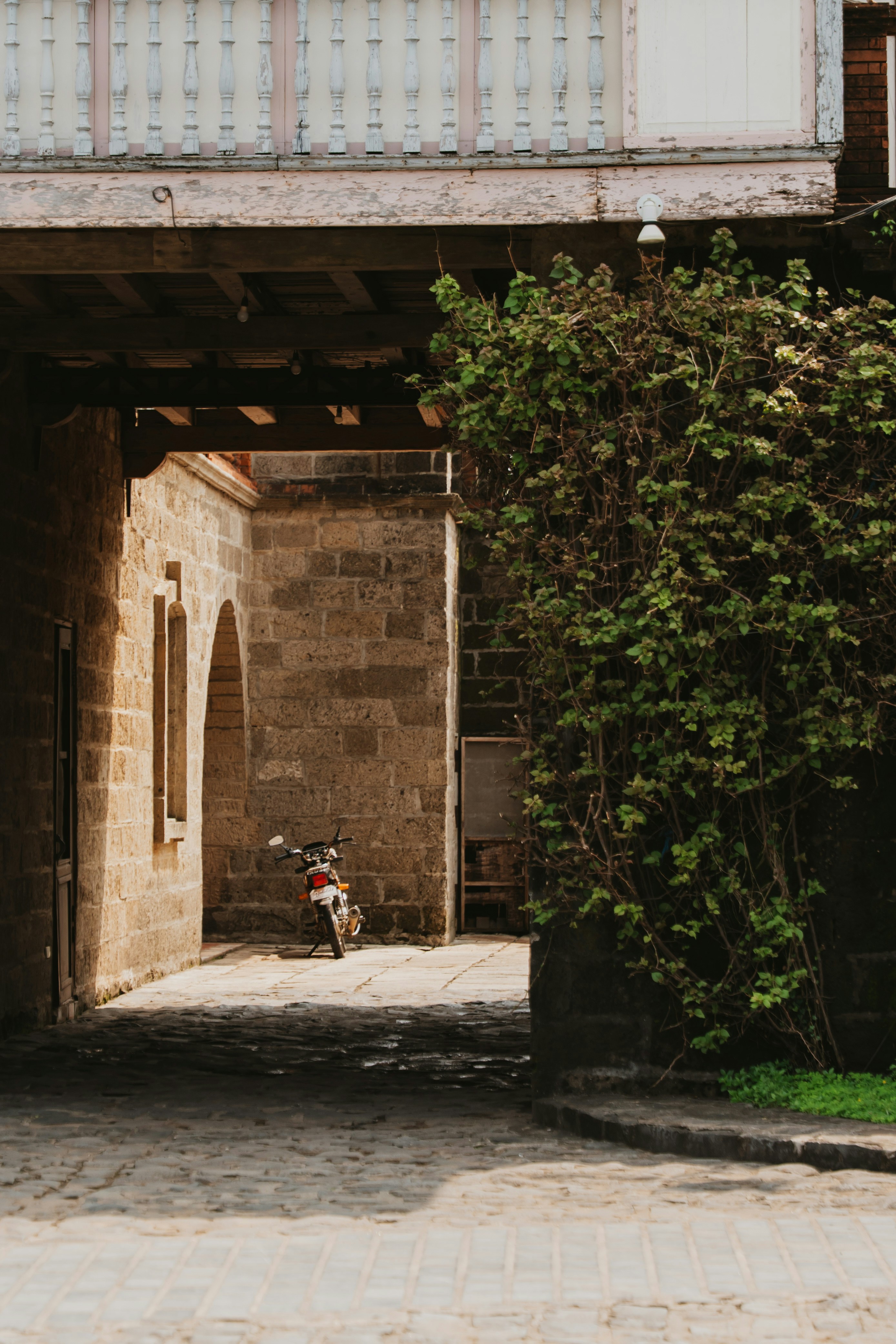 A motorcycle parked in a sunlit stone archway beside a leafy green vine