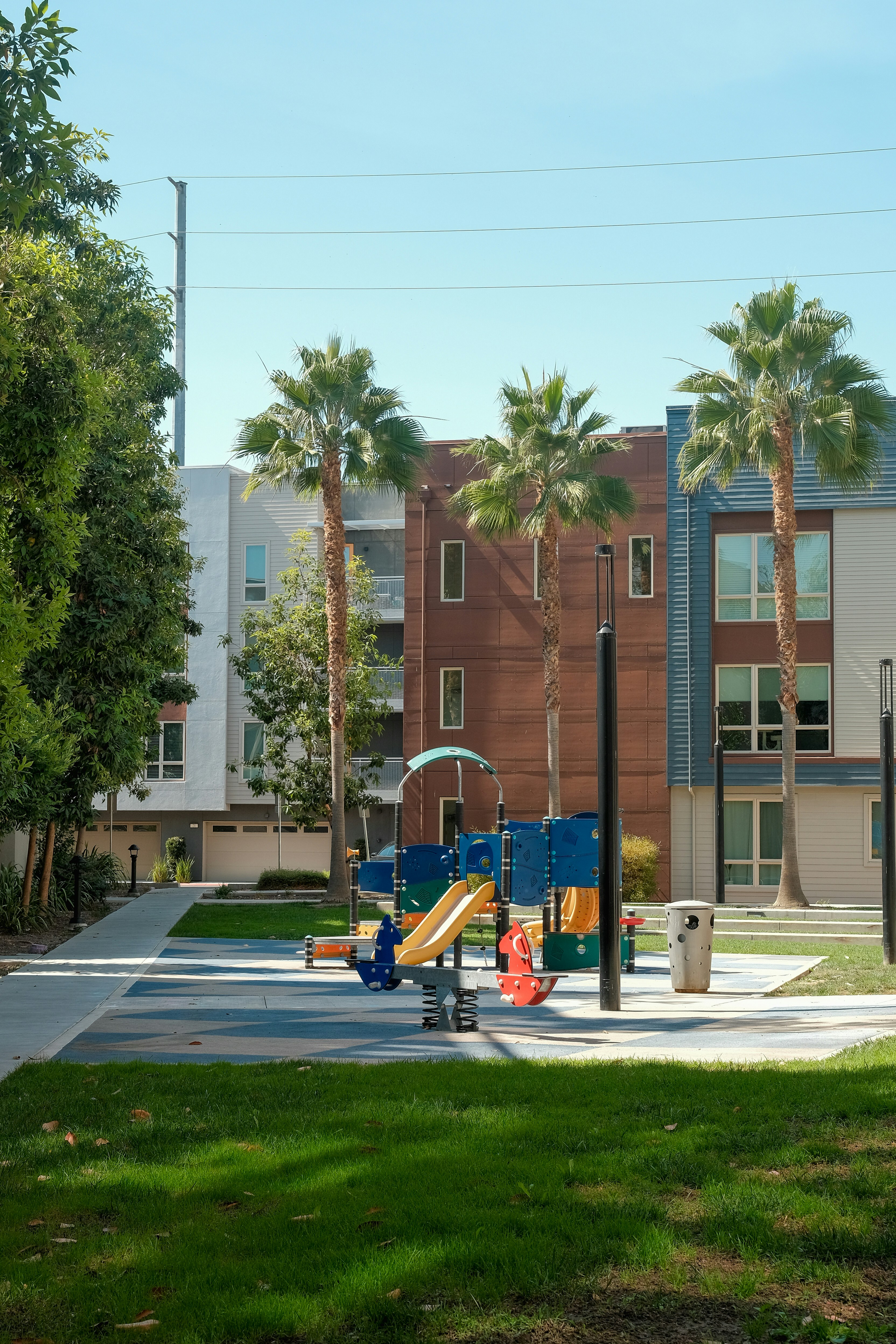 A colorful playground with slides and a seesaw near palm trees and apartment buildings