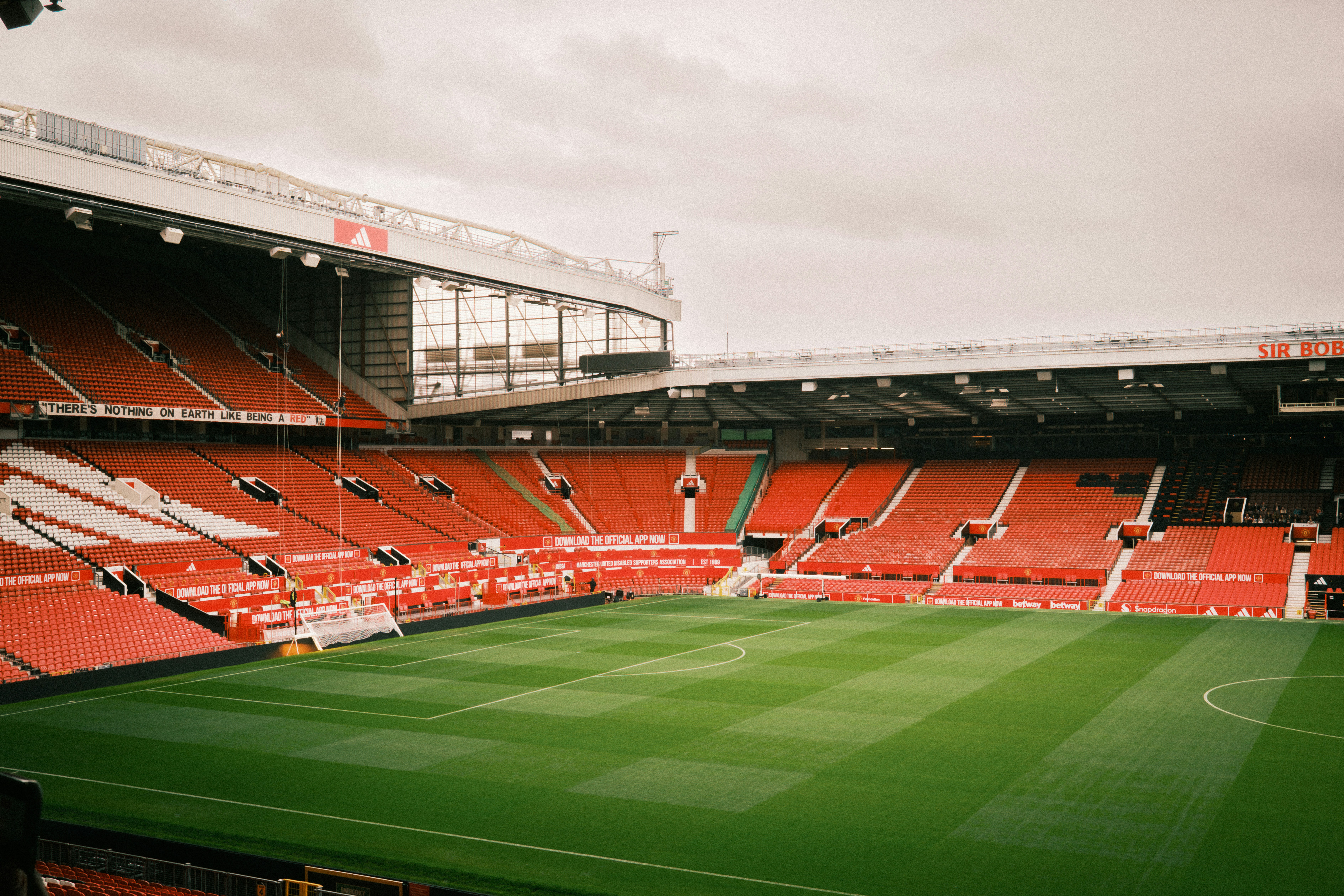 Stade de football vide aux sièges rouges, pelouse verte sous un ciel couvert