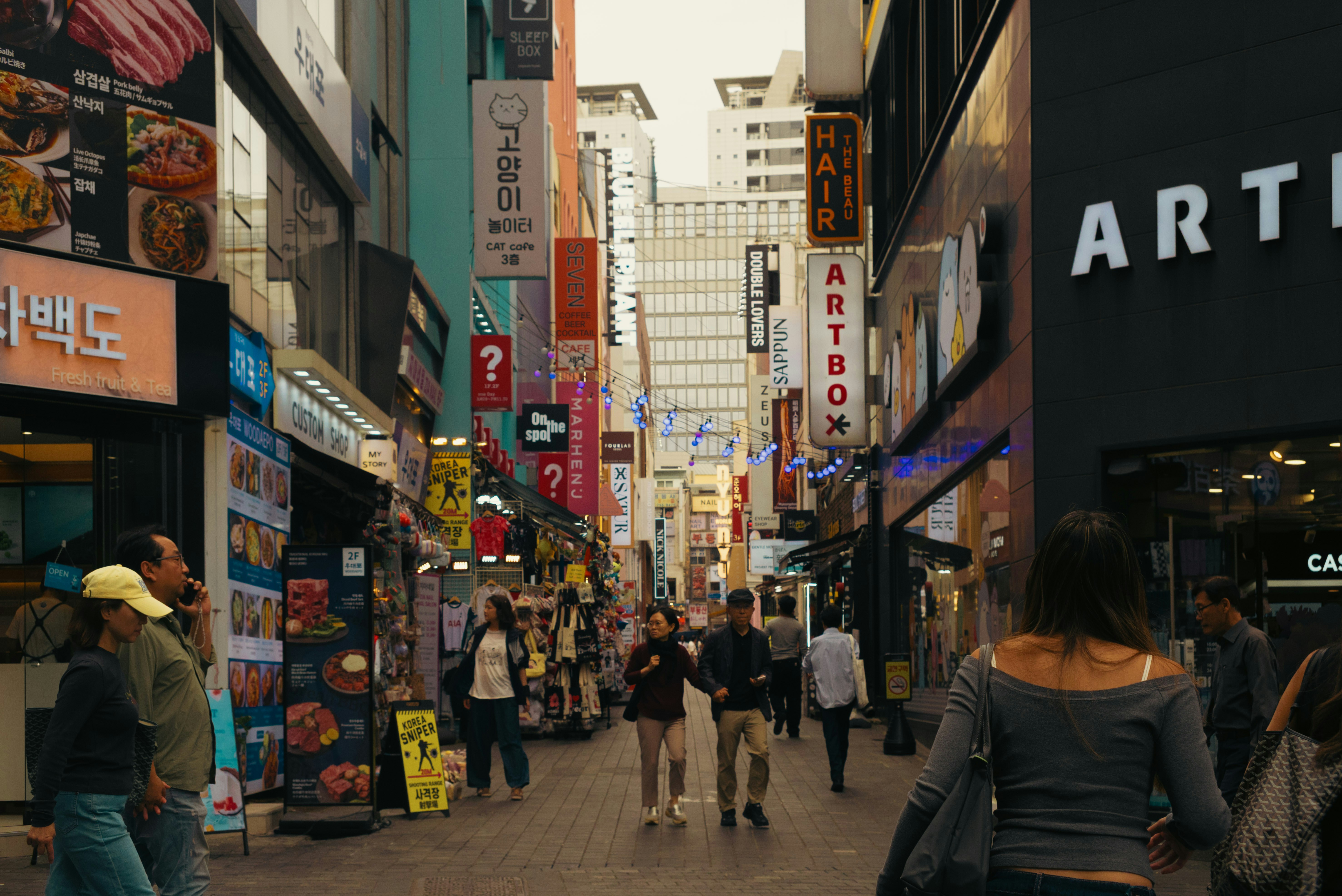 People walking along a narrow street in Seoul lined with colorful shop signs