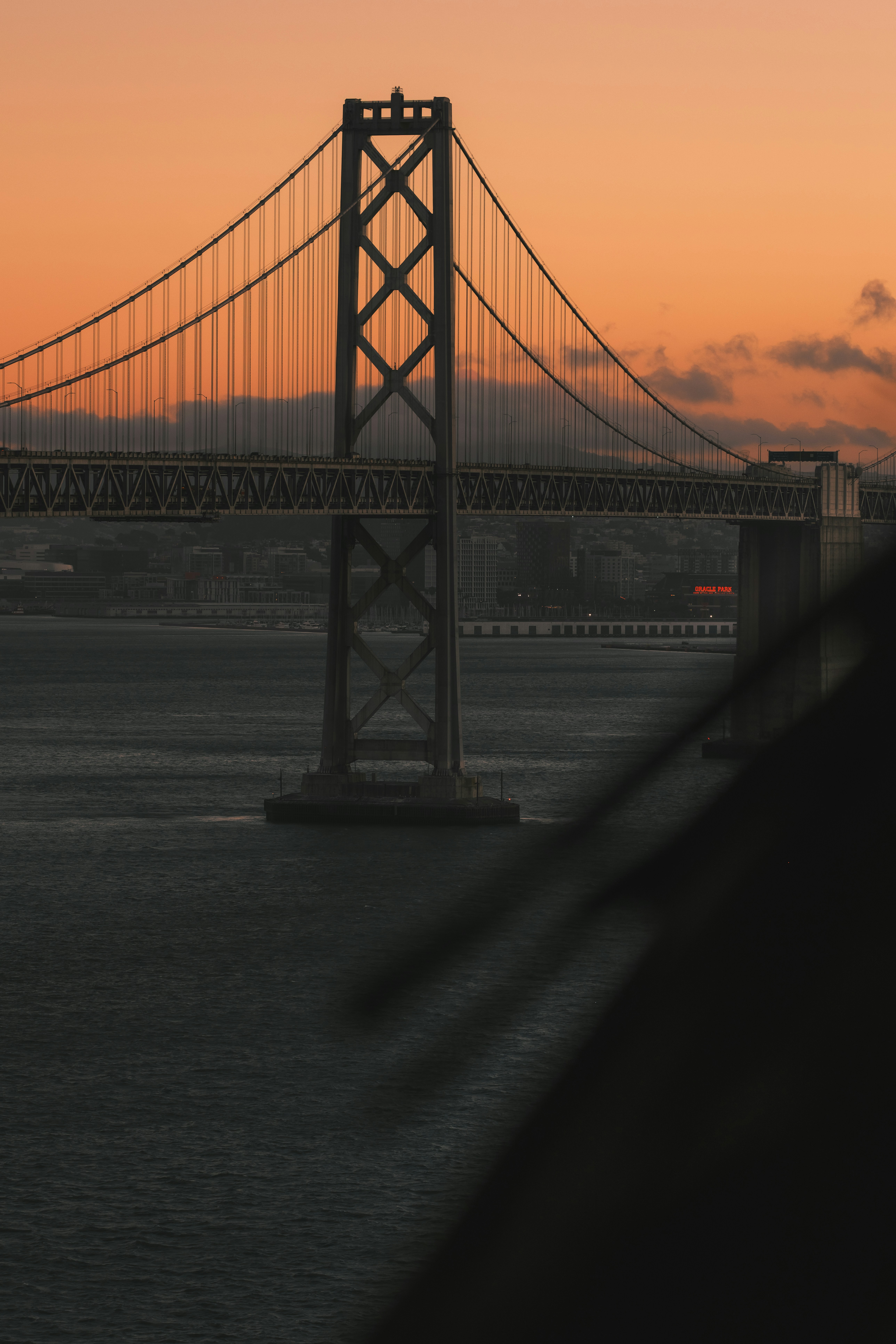 The Bay Bridge in San Francisco under a warm orange sky at golden hour