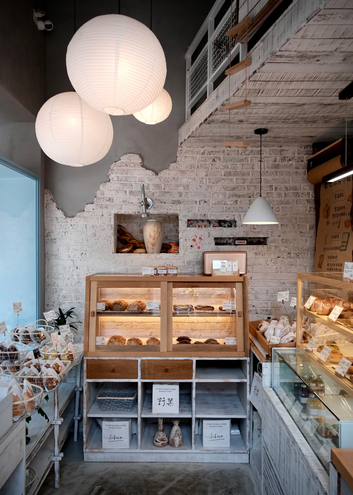 The bakery room: a white brick wall, a paper lantern and a wooden case of bread by the window