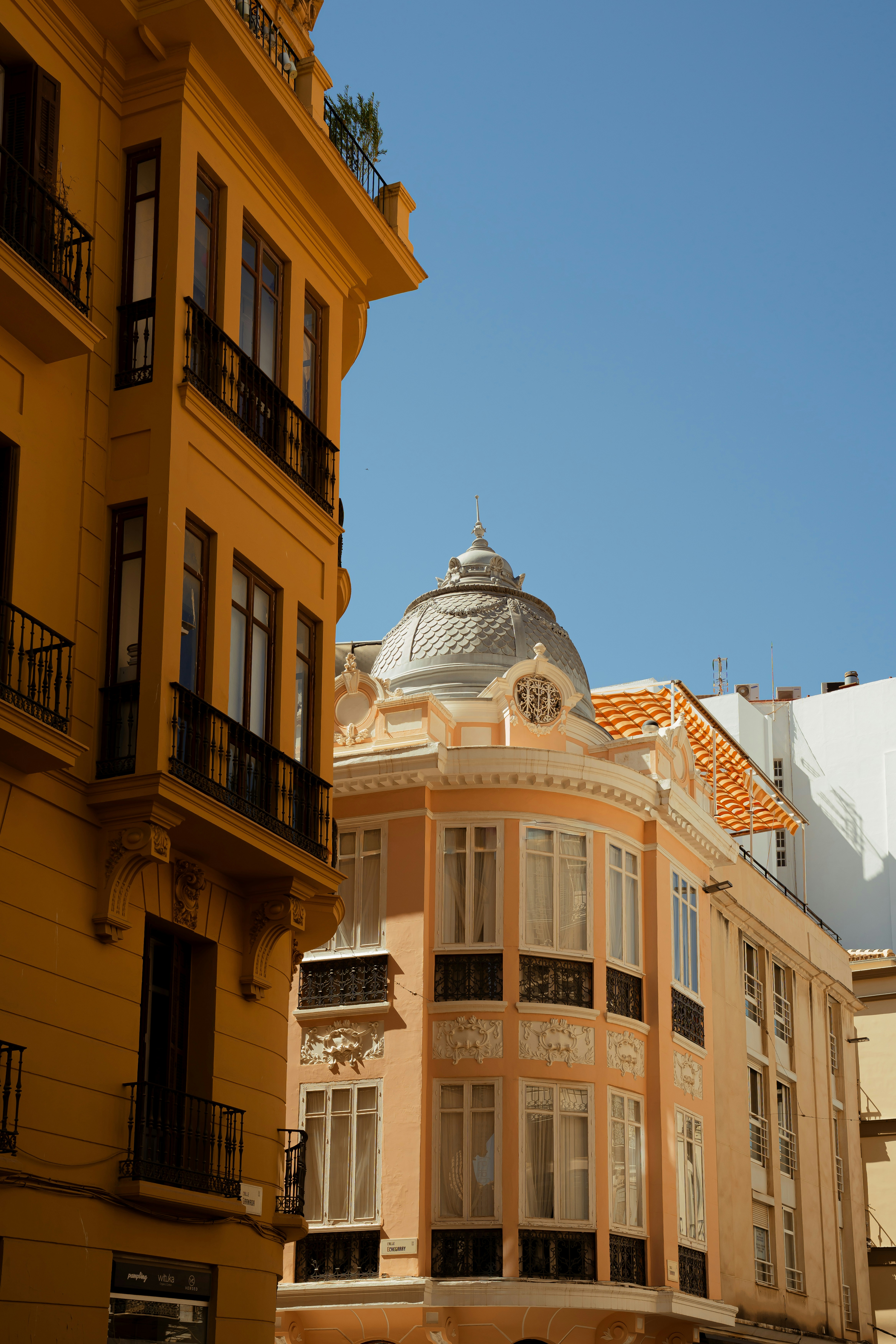 A yellow building and a peach building with ornate balconies under a clear sky