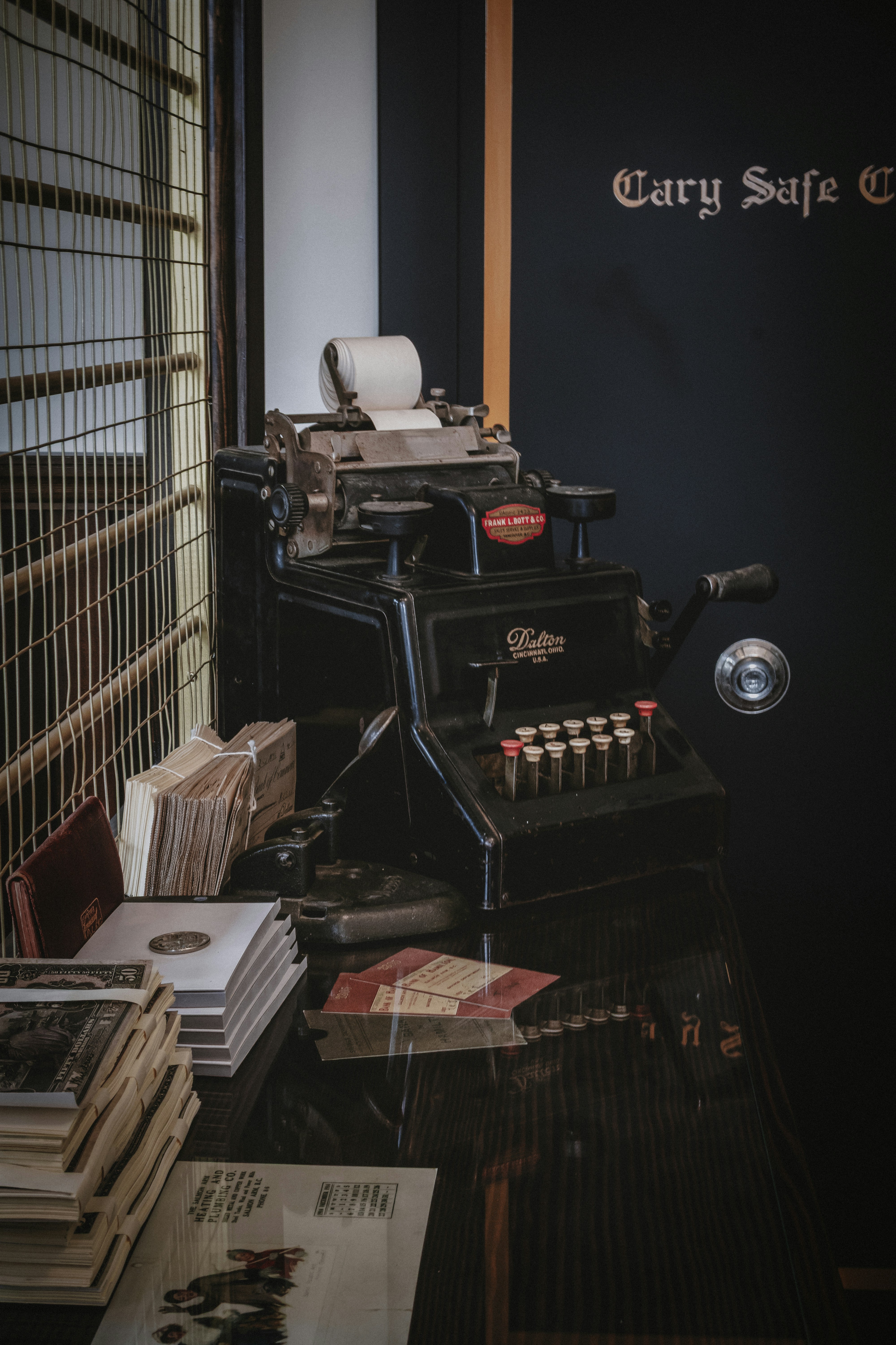 A vintage Dalton adding machine on a dark wooden desk with stacks of paper