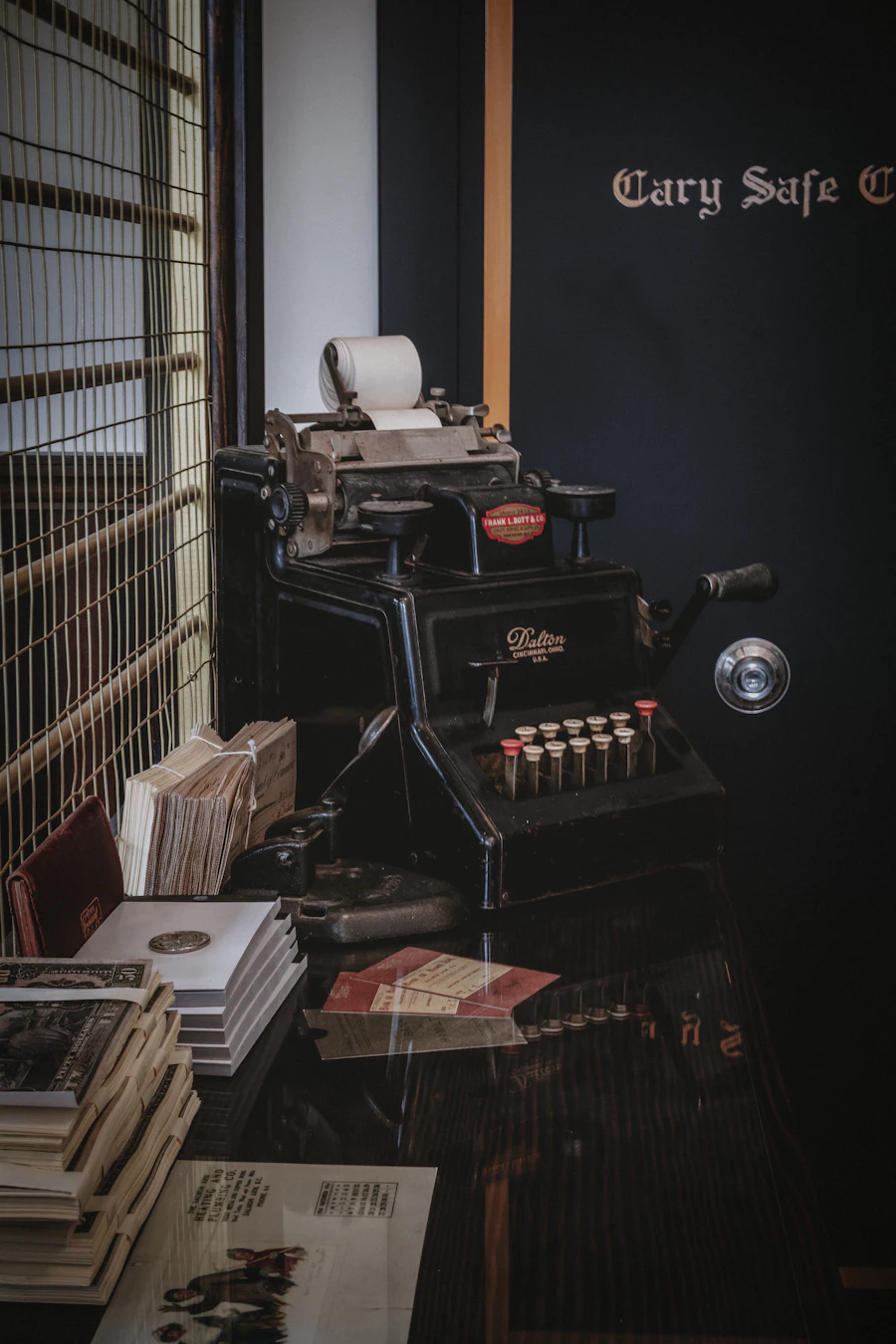 A vintage adding machine on a wooden desk with paperwork