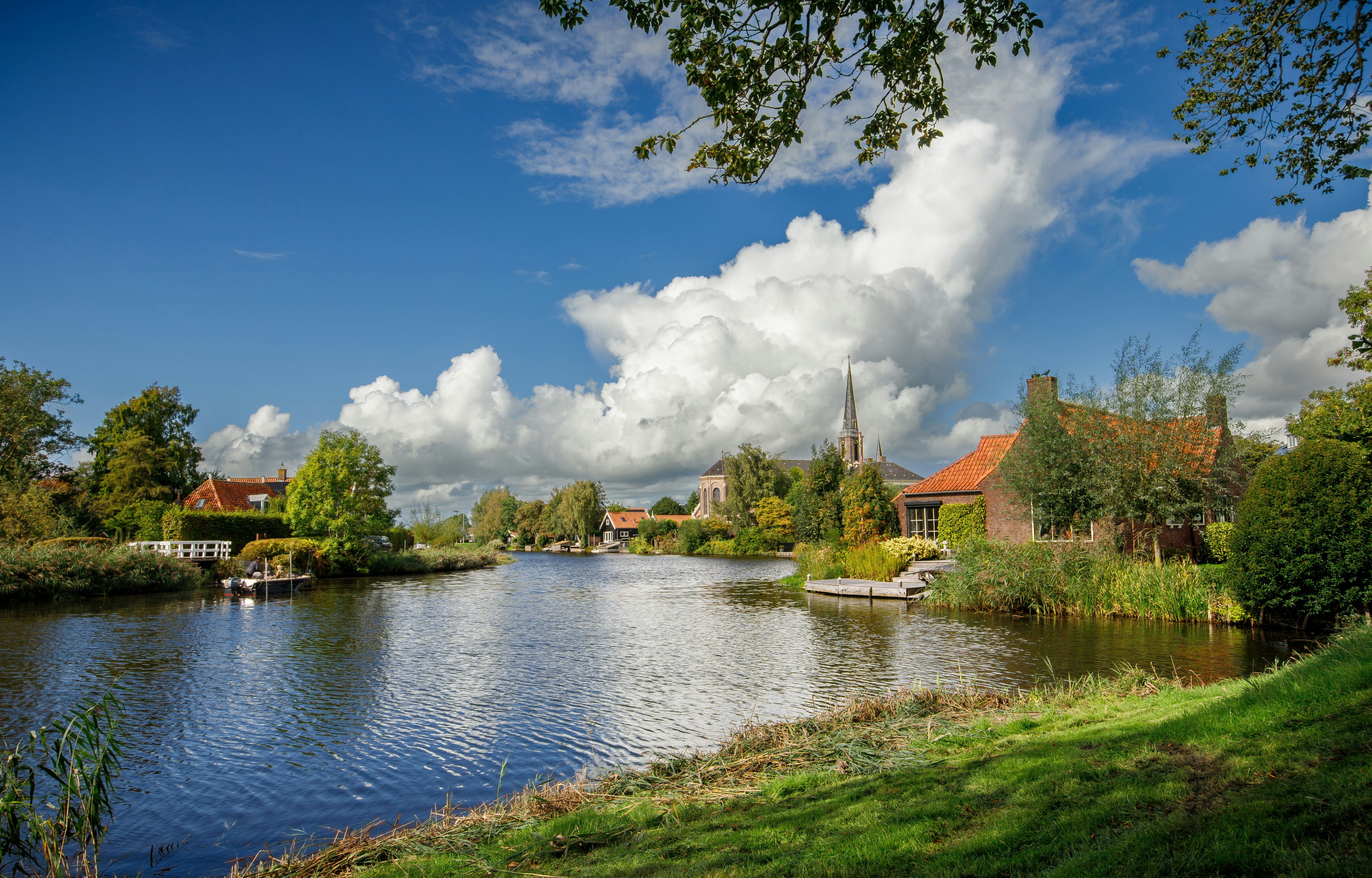 A canal flowing past brick houses and a church spire under a cloudy sky