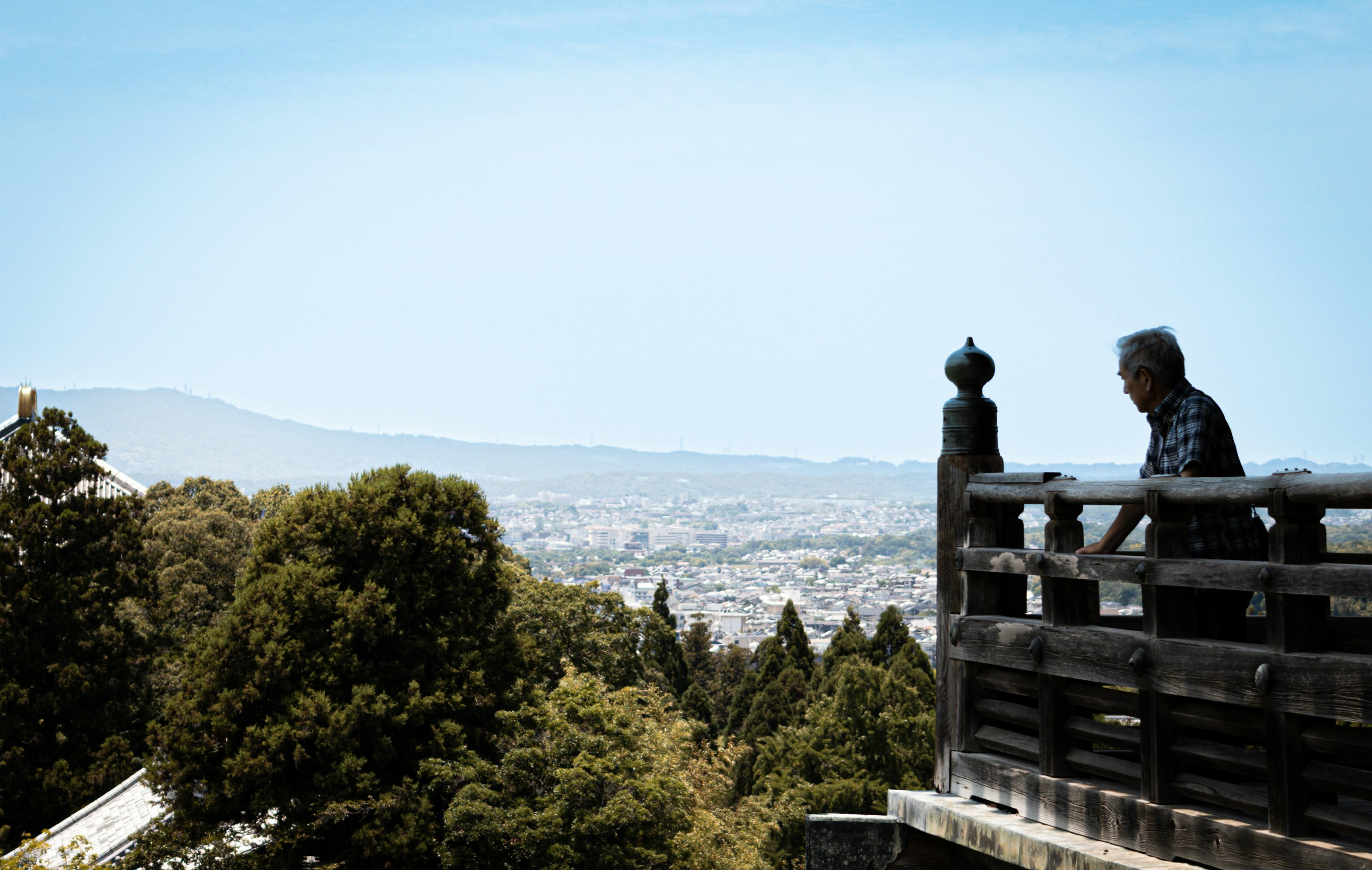 An adult looking over a city from a wooden balcony in Japan