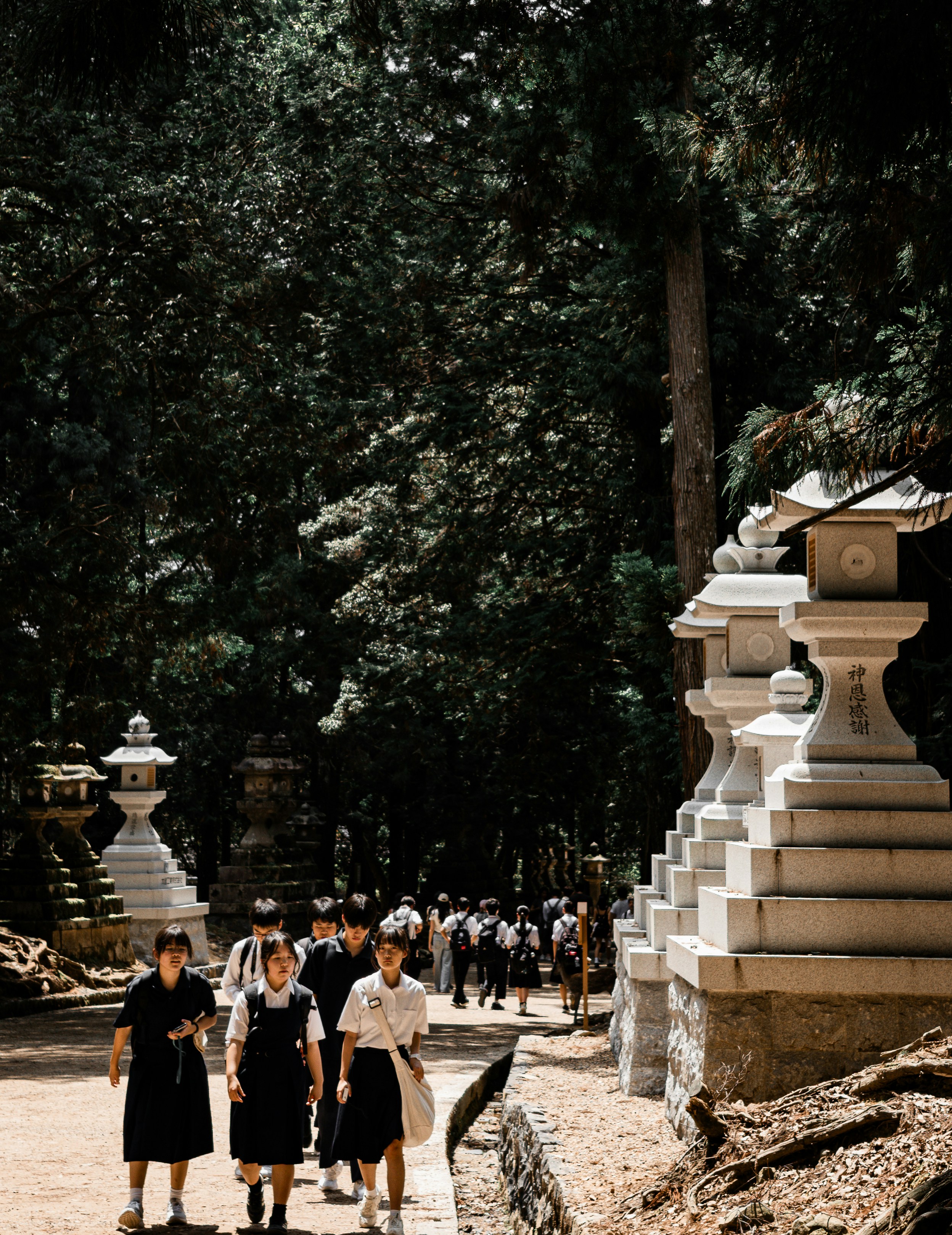 Students in school uniforms walking along a path lined with stone lanterns