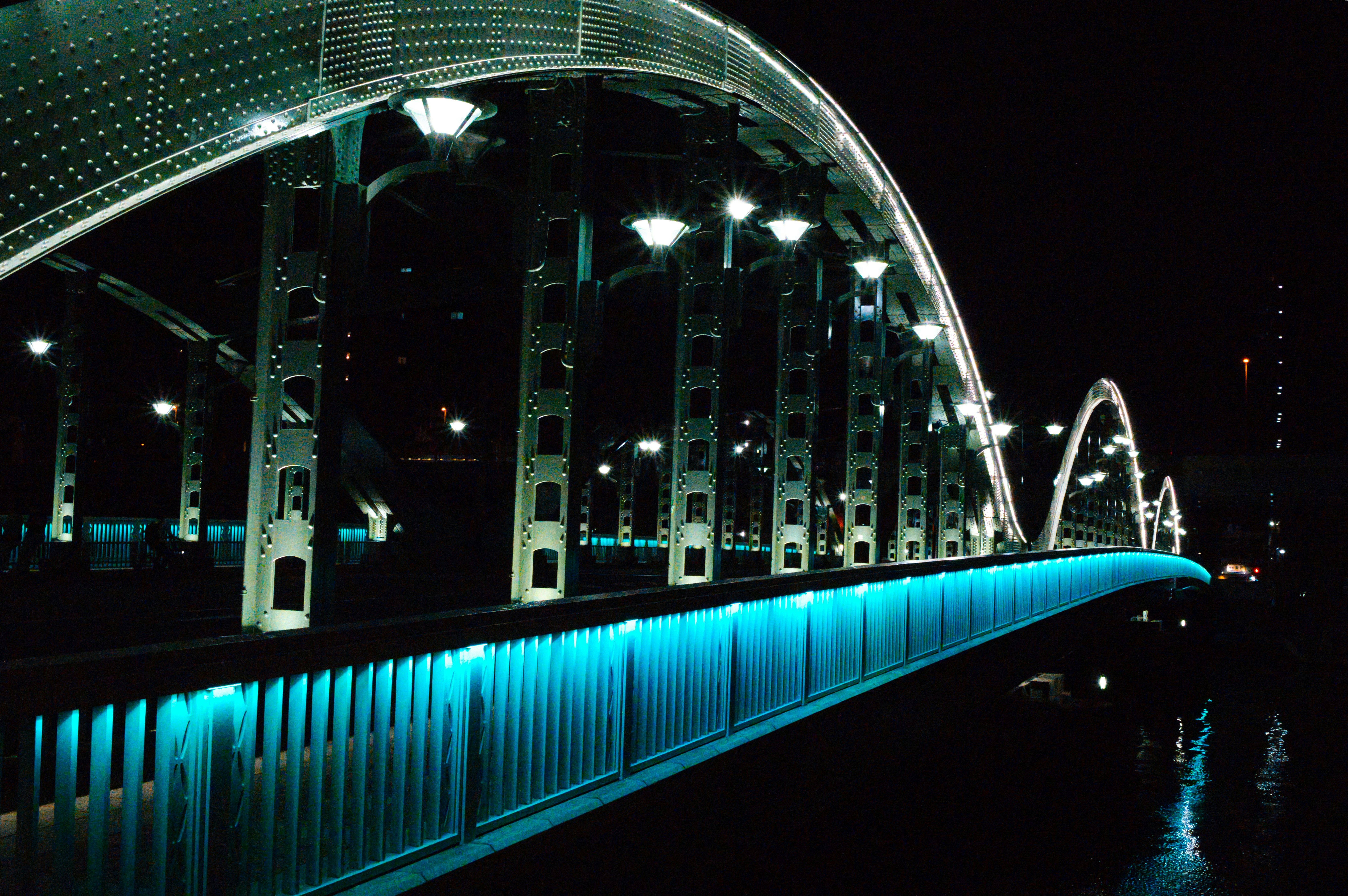 An arched metal bridge illuminated with bright blue lights at night