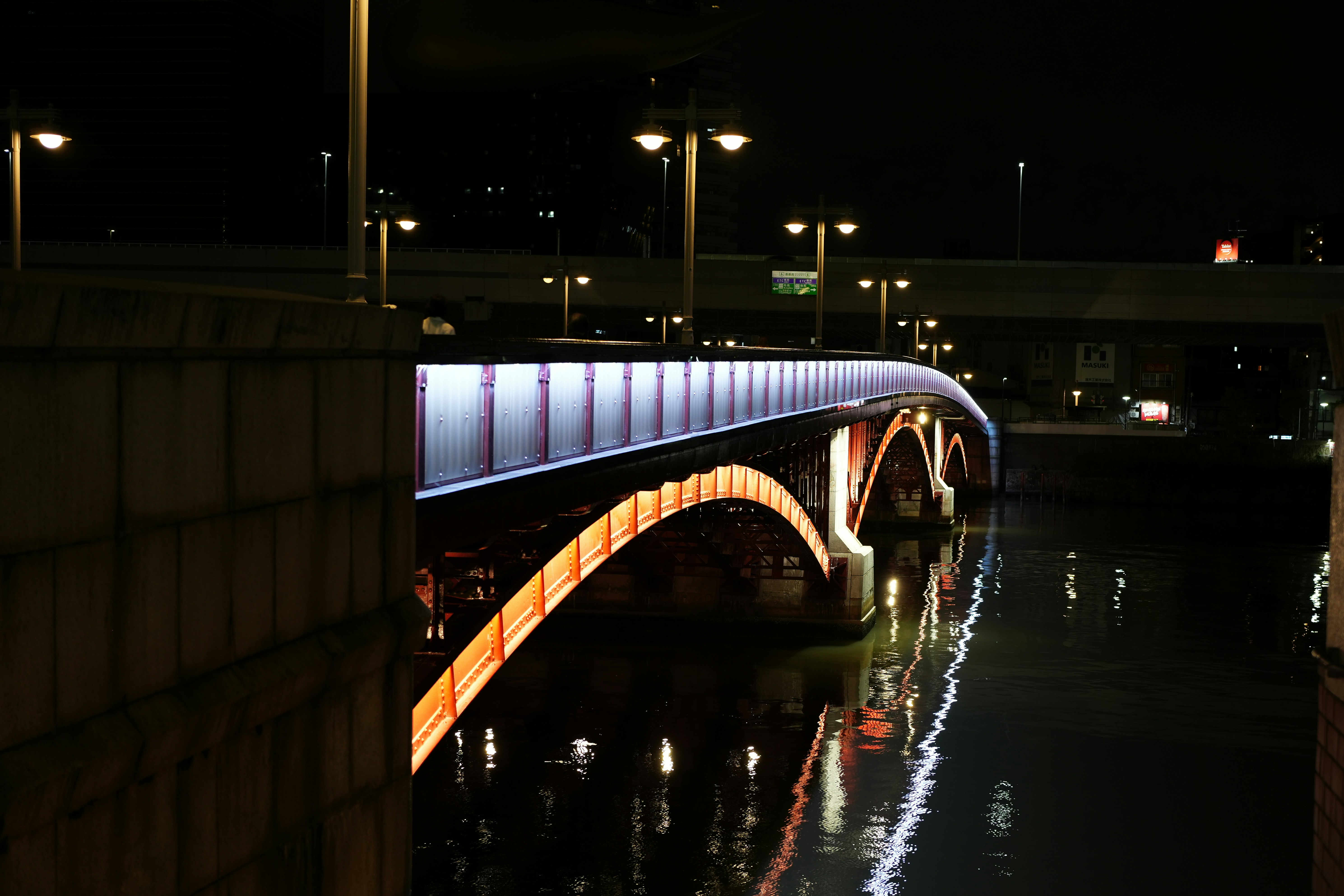 An illuminated arched bridge over a dark river at night with street lamps