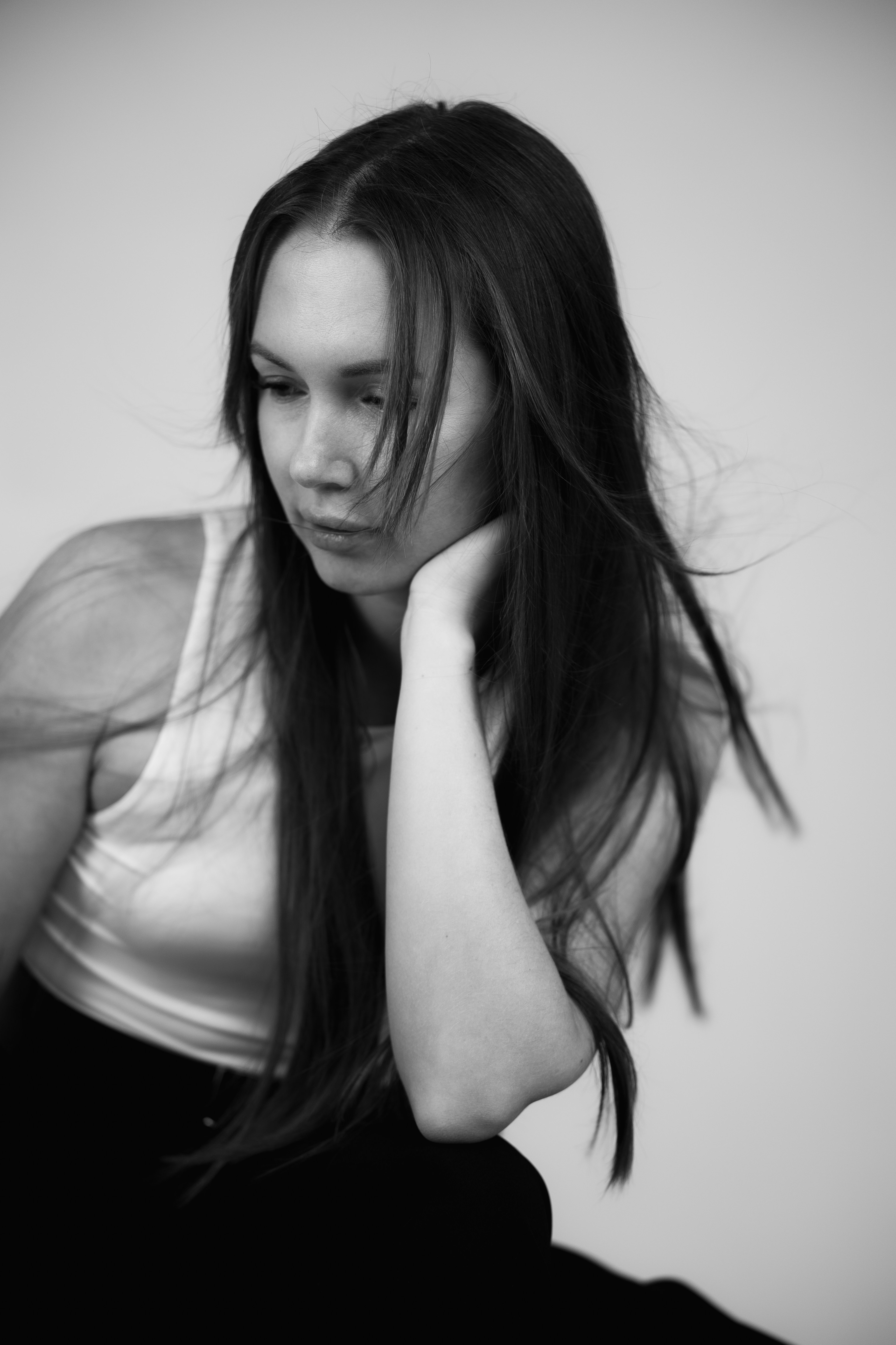 A woman with long hair in a white tank top looking down