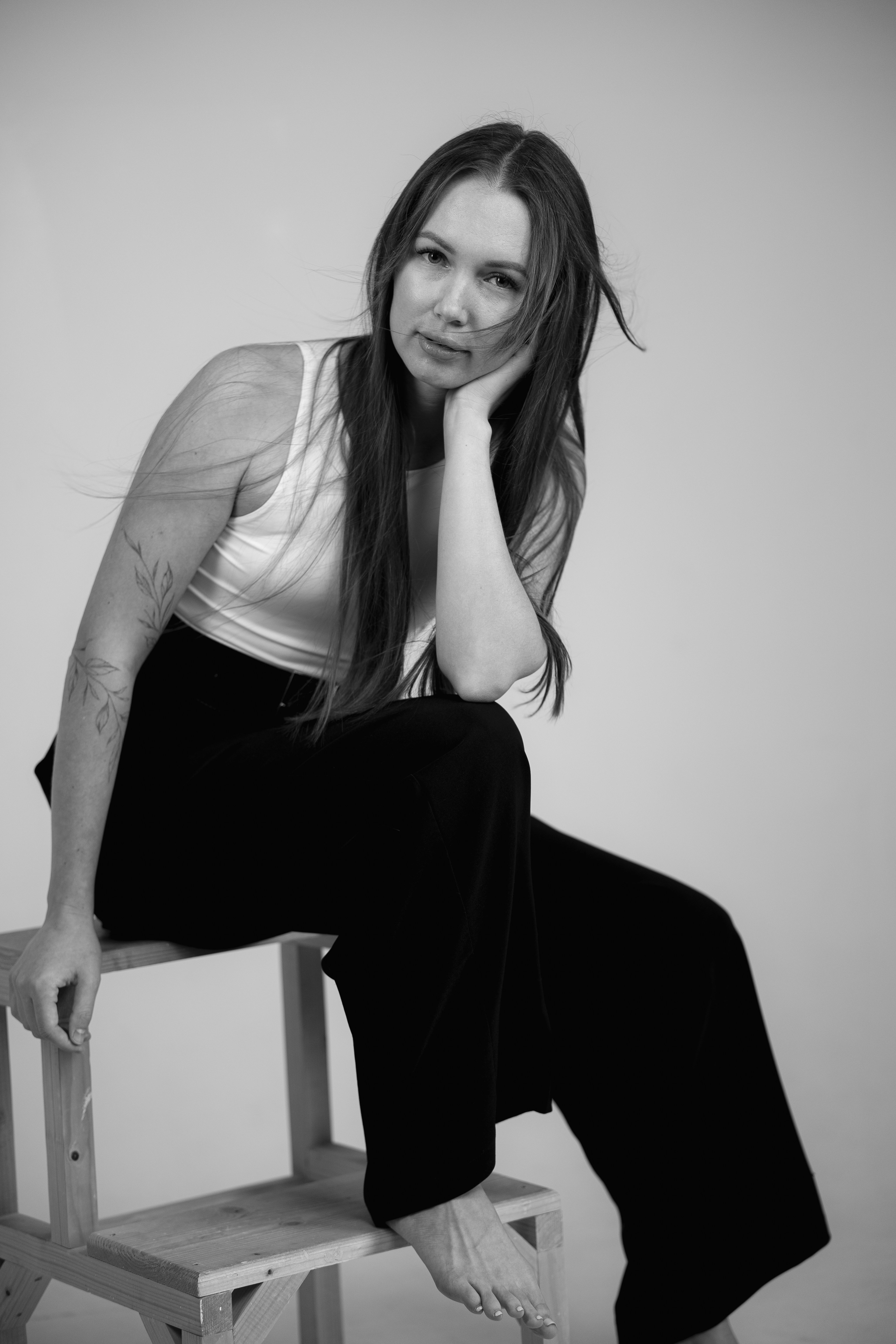 A woman in a white tank top and black trousers sitting on a stool