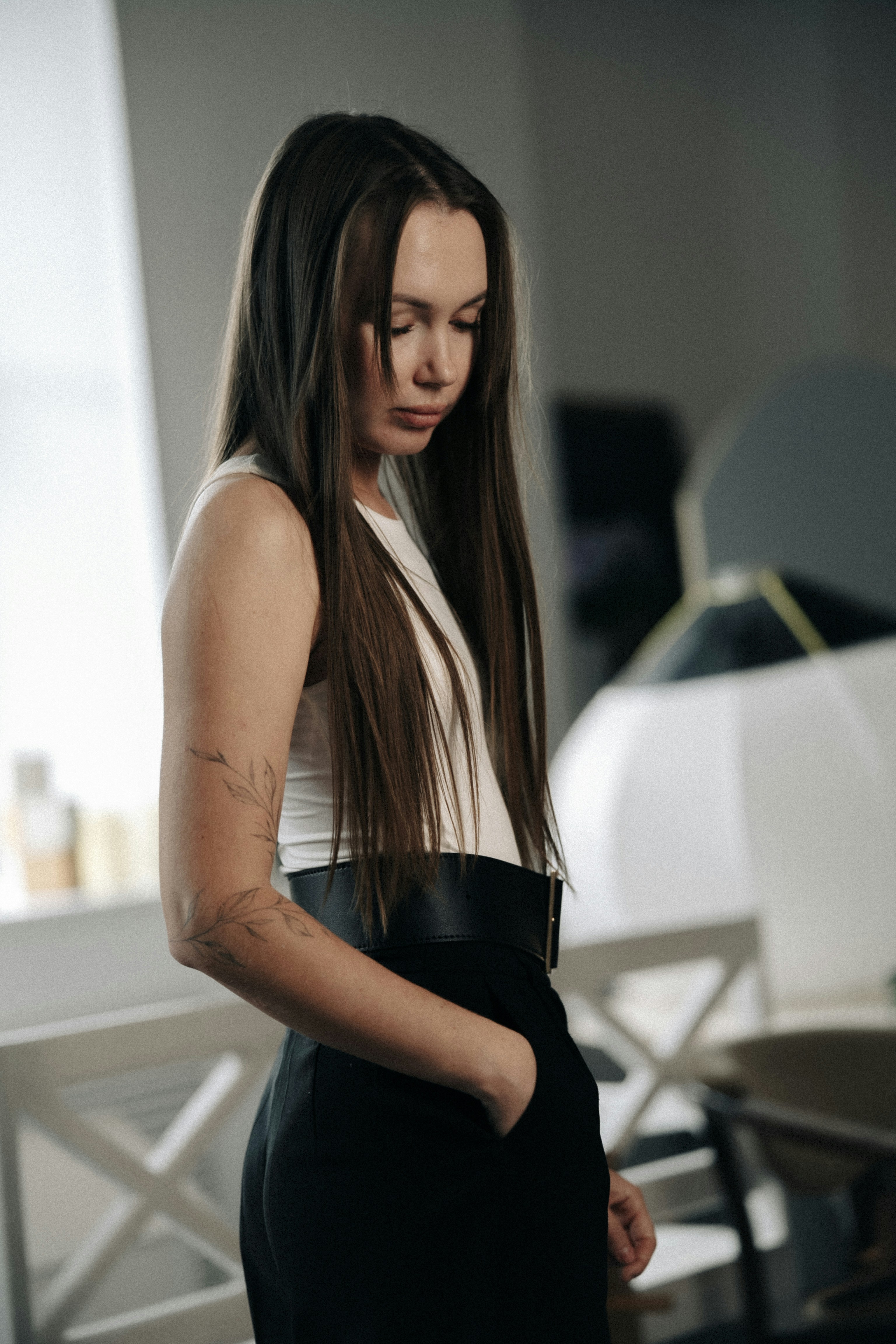 A woman with long brown hair and a floral arm tattoo in a white top