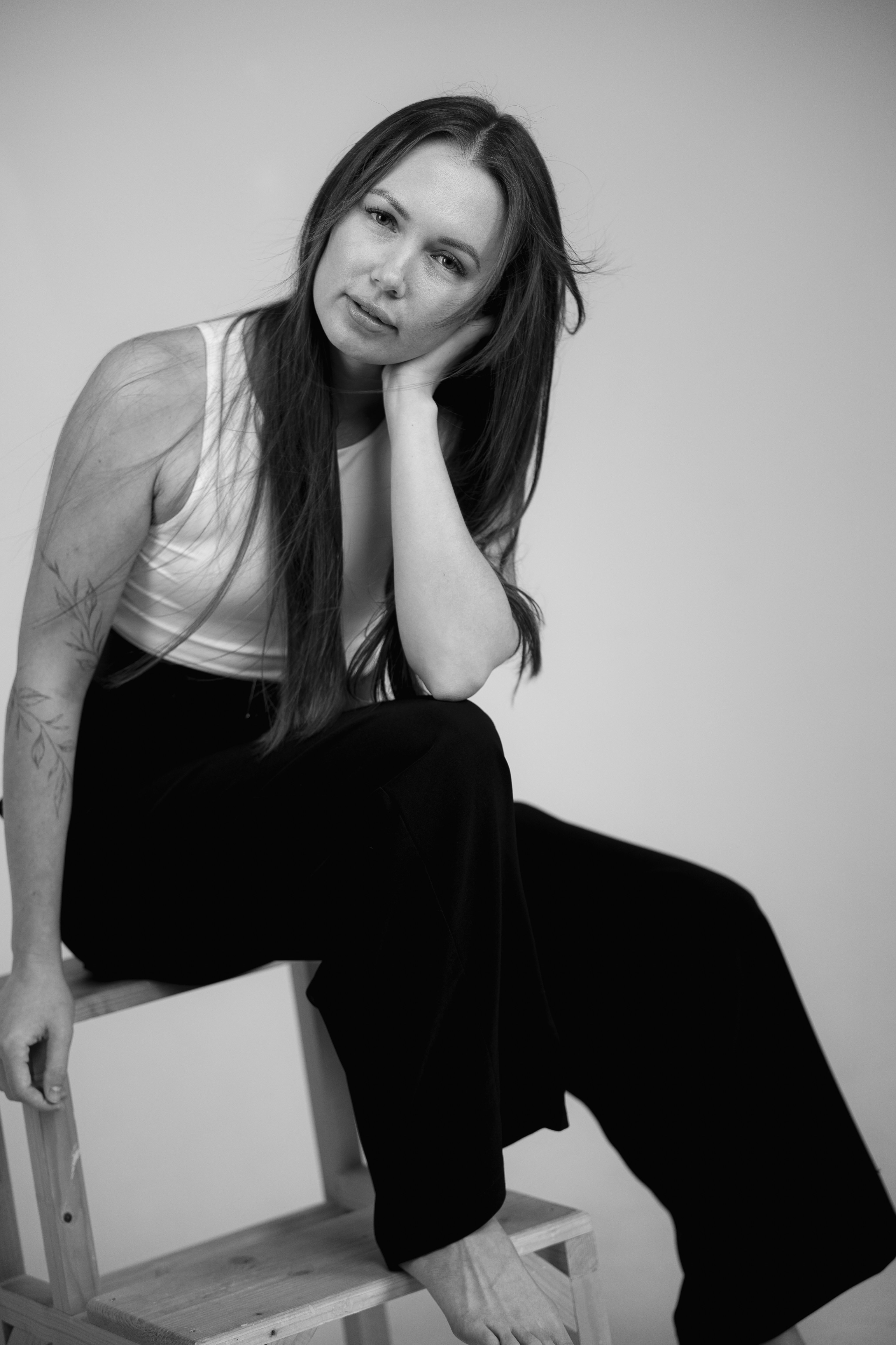 A woman with long hair and a floral arm tattoo in a white tank top