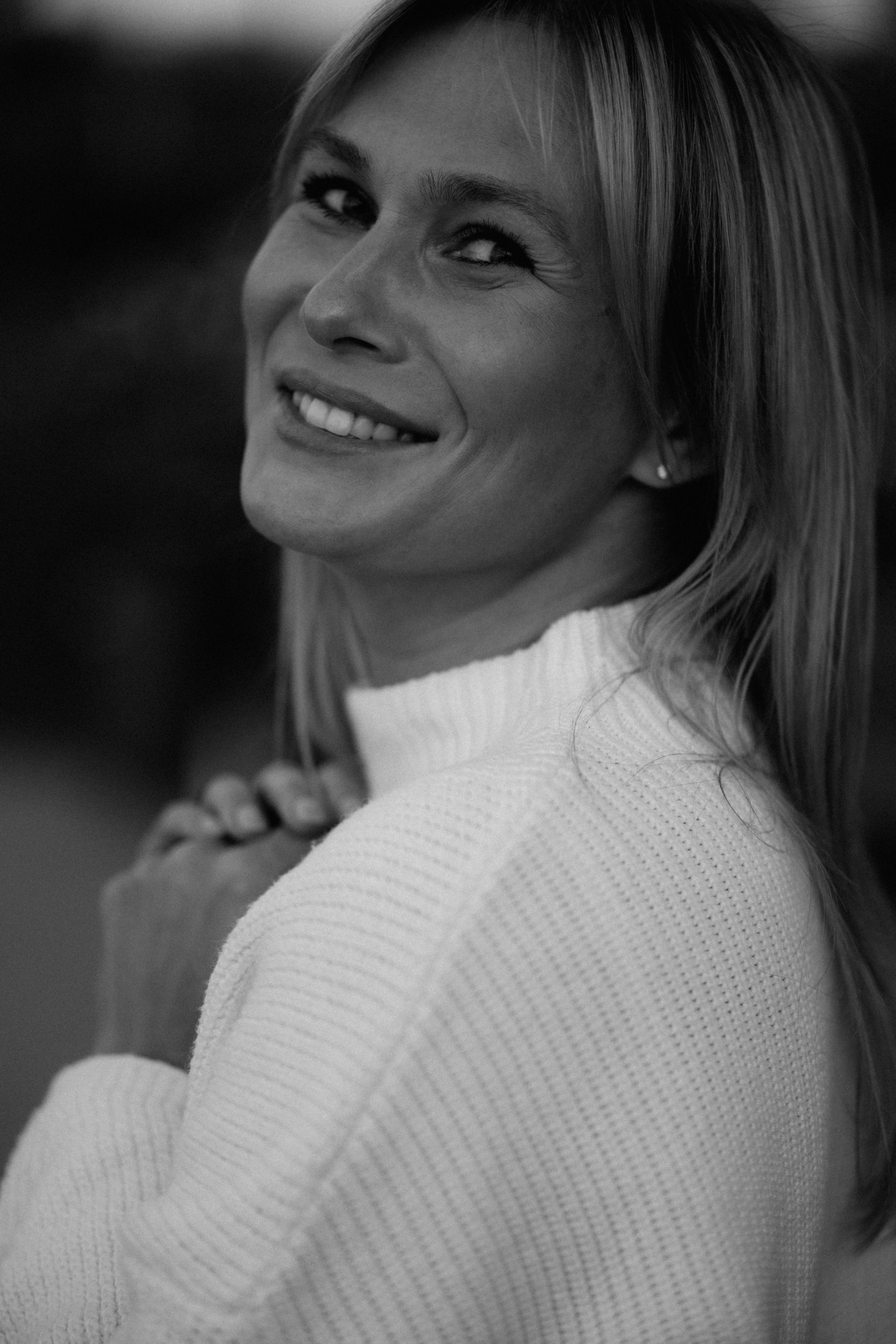 A smiling woman with blonde hair wearing a white ribbed sweater