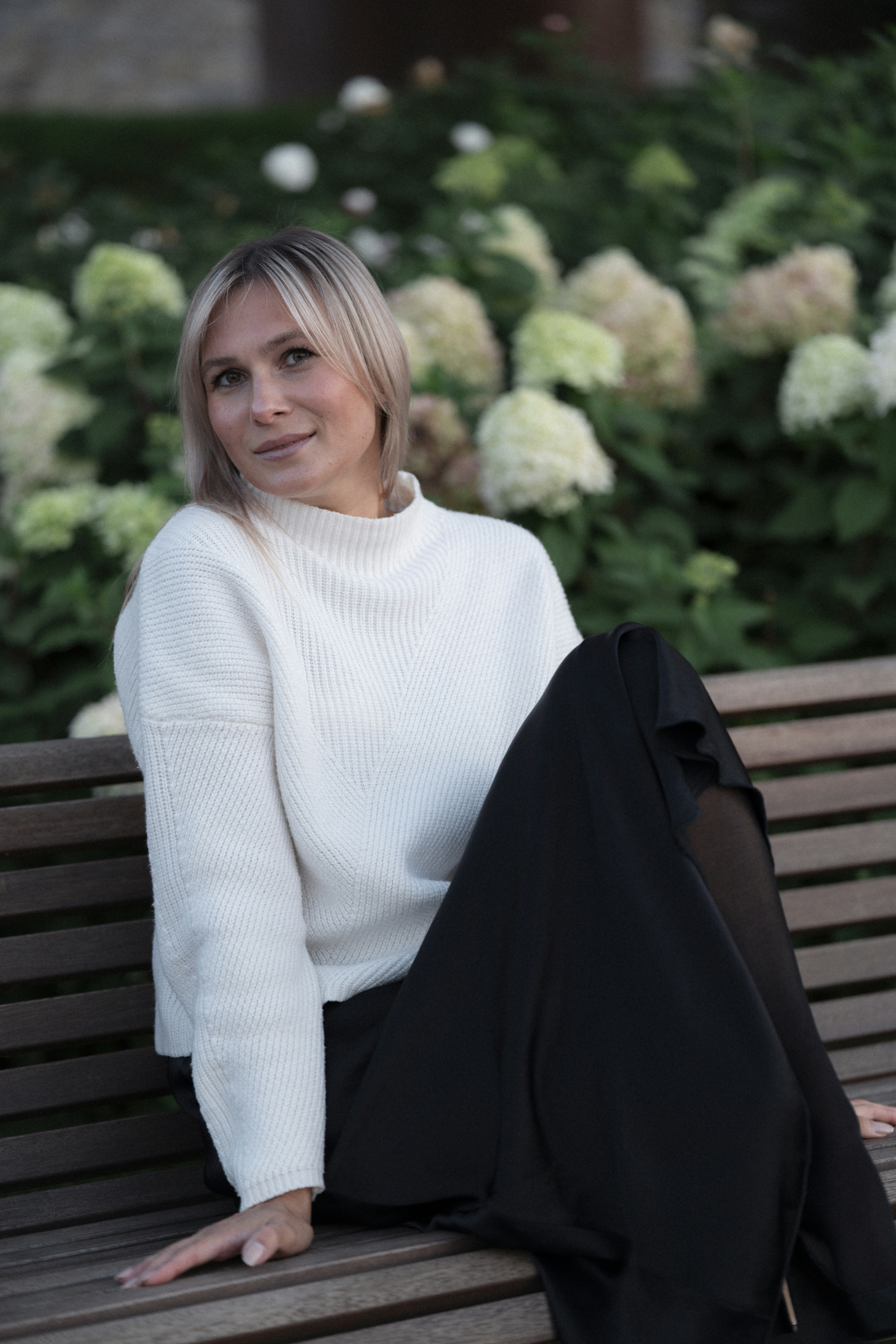 A woman in a white sweater and black skirt on a wooden bench