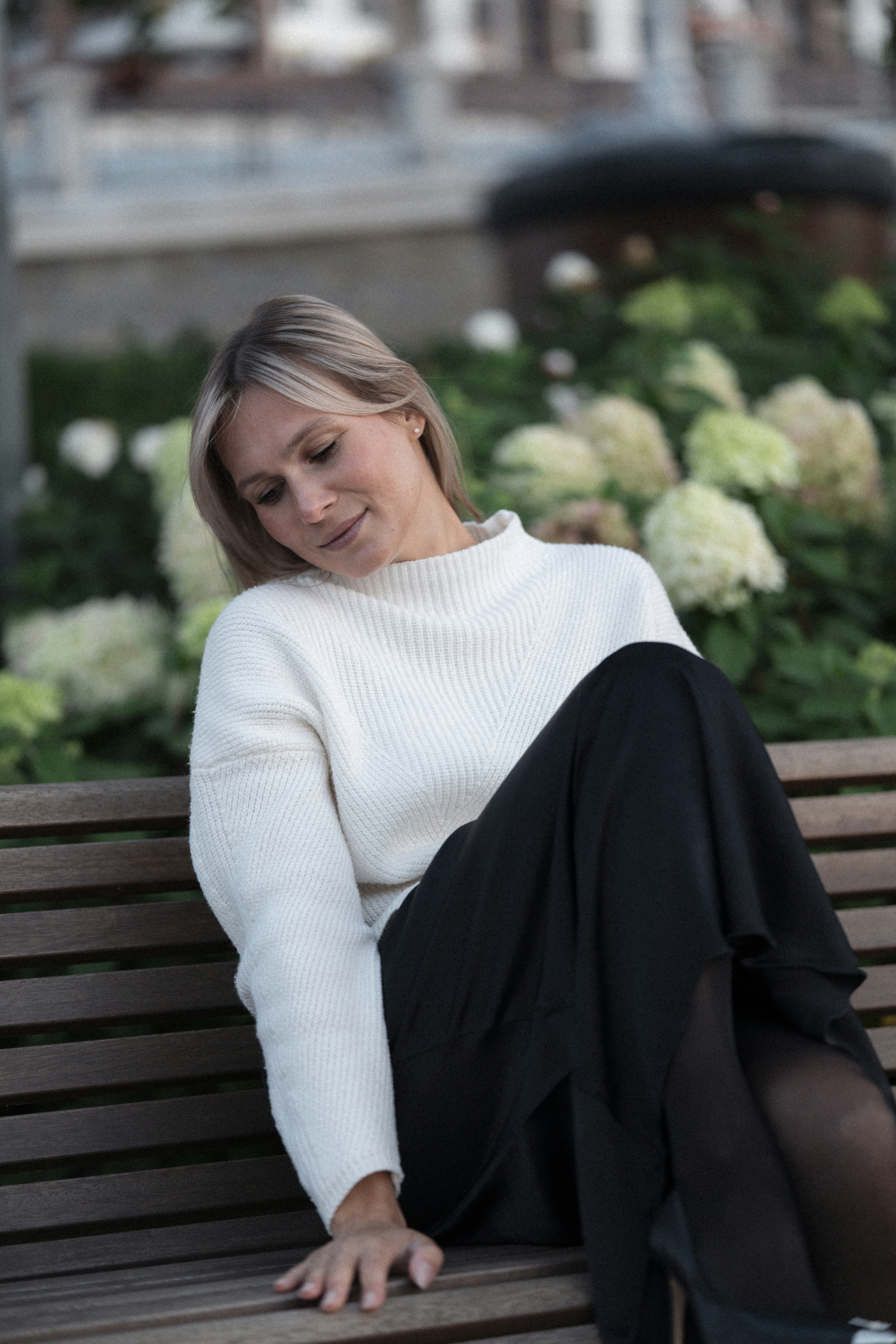 A woman in a white sweater and black skirt sitting on a wooden bench