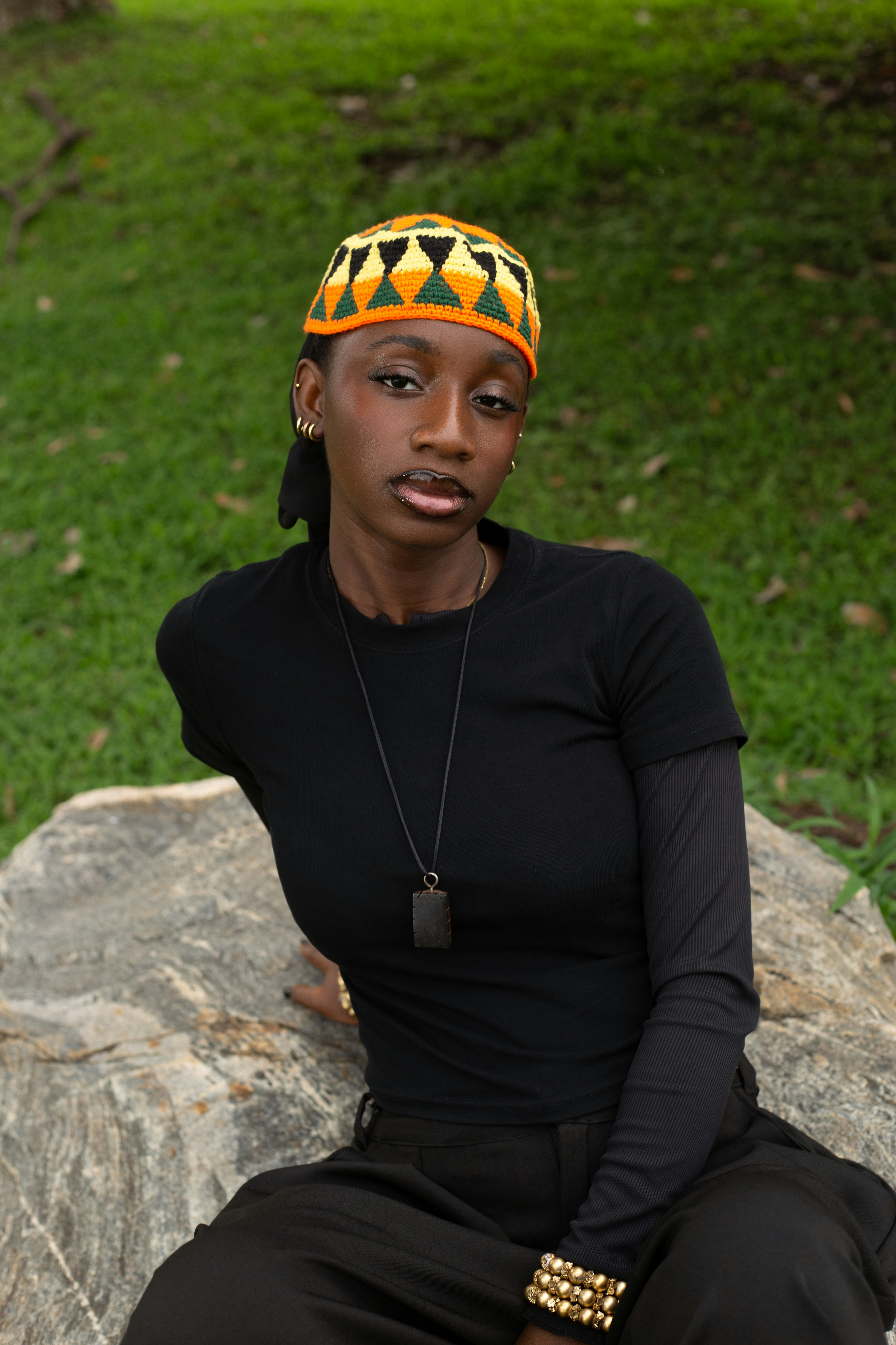 A woman in a black shirt and patterned beanie sitting on a large rock