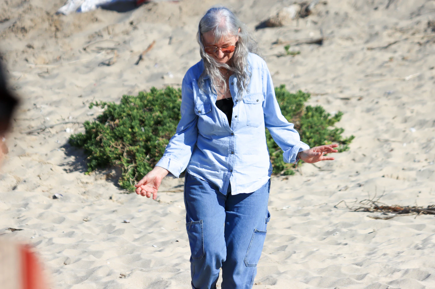 A woman with long gray hair walking on a sandy beach