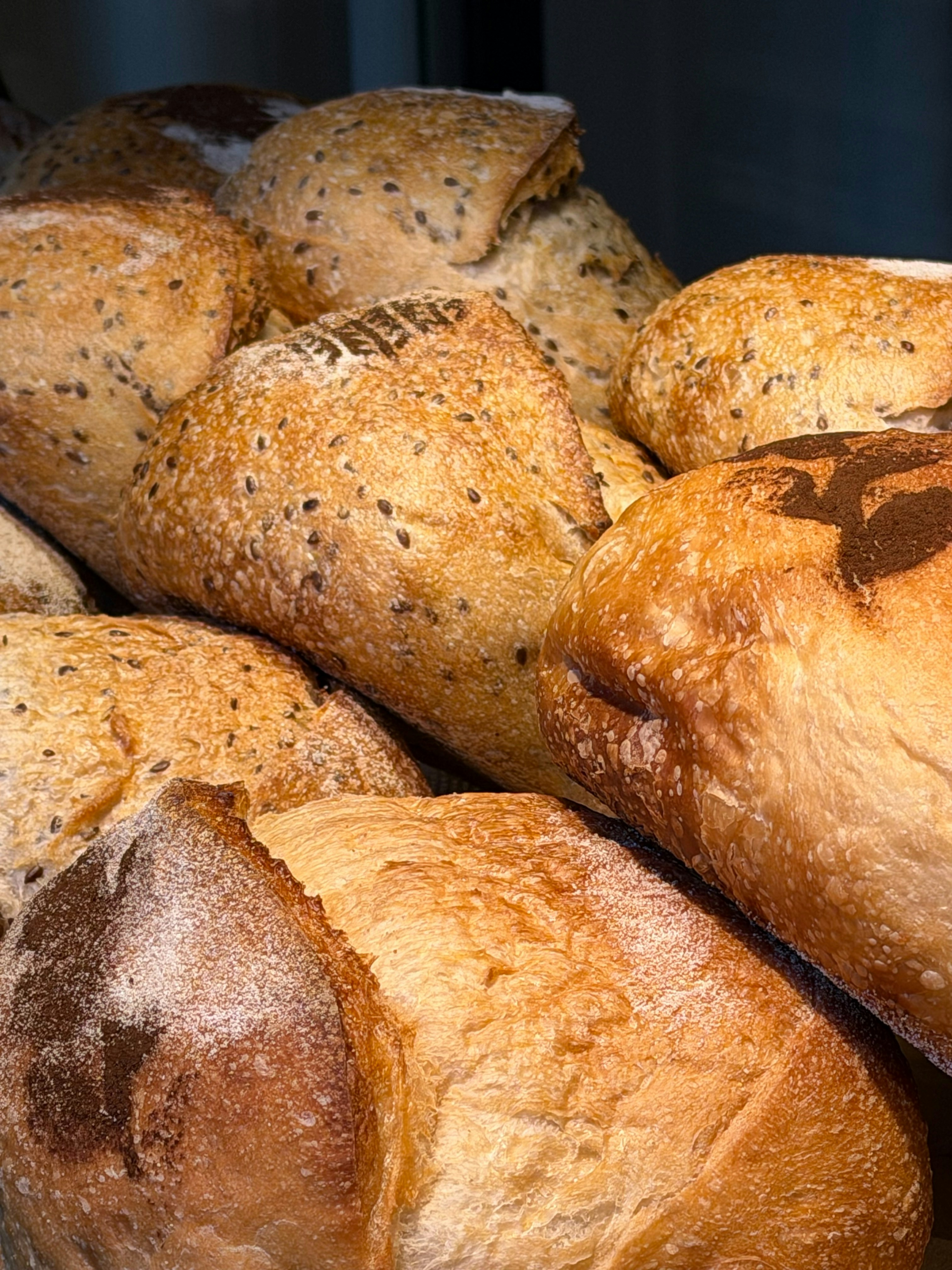 A pile of golden brown artisan loaves with seeds and flour dusting