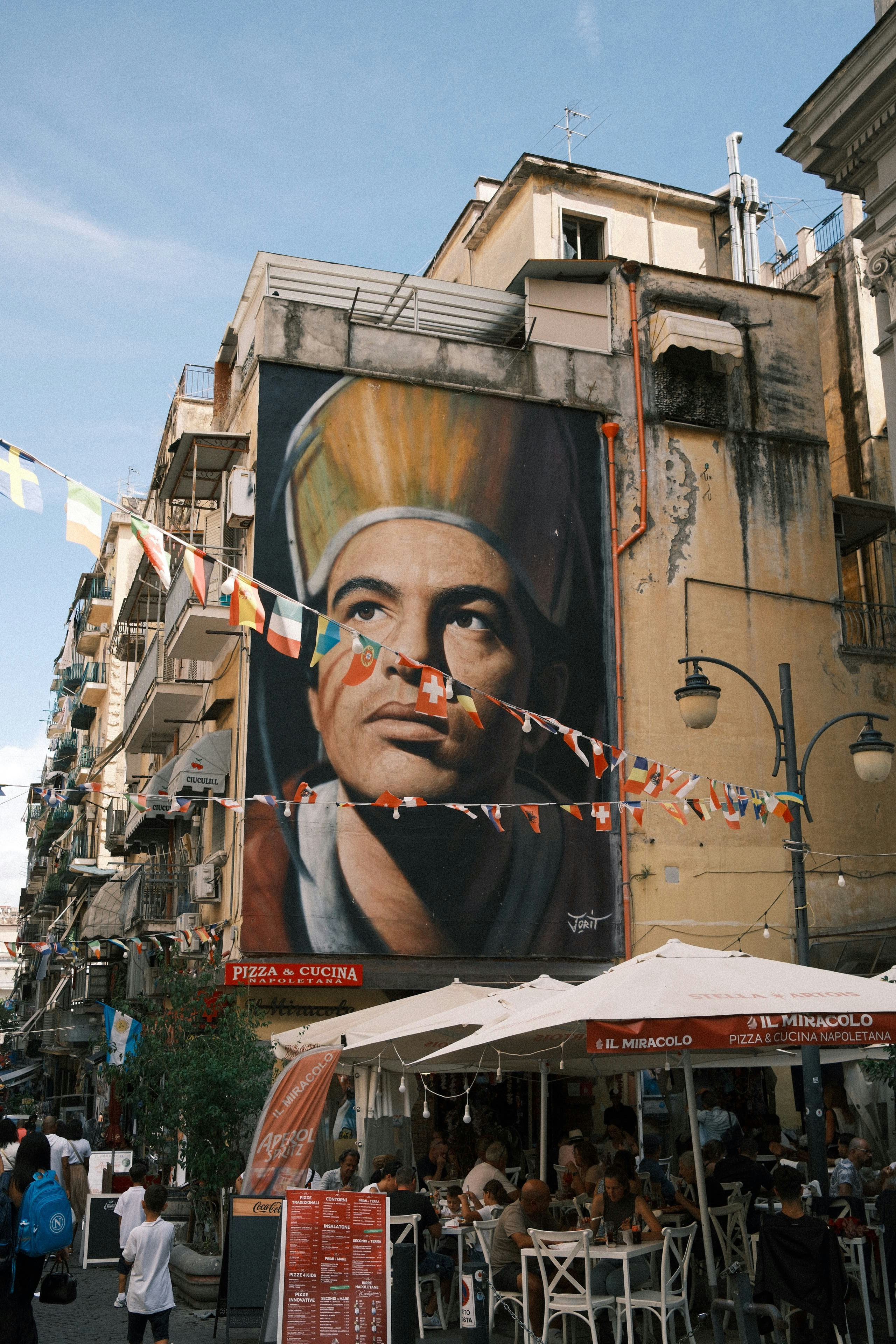 A large mural of a man on a building facade above a busy outdoor restaurant
