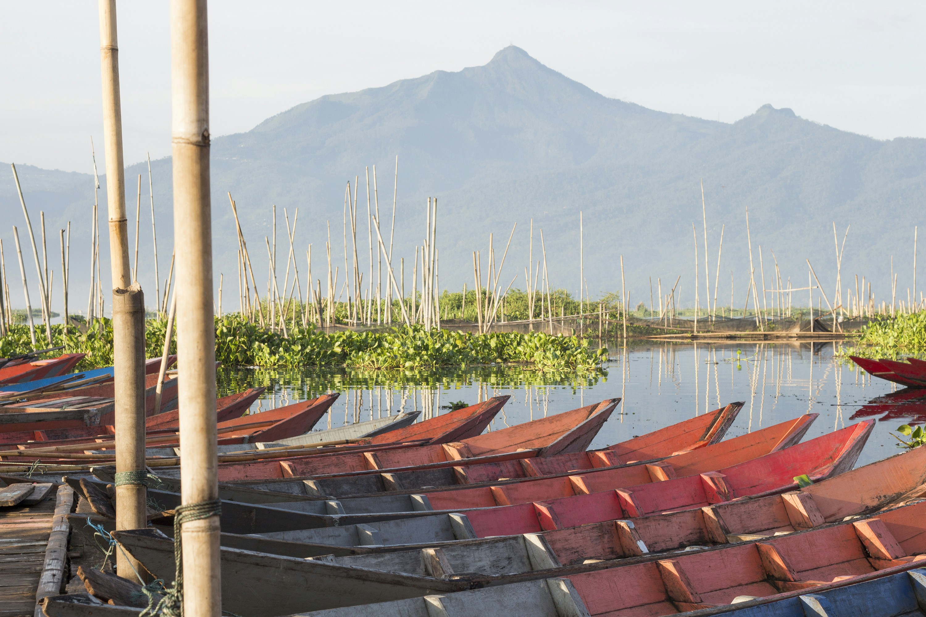Red wooden boats moored at a bamboo dock before a misty mountain lake