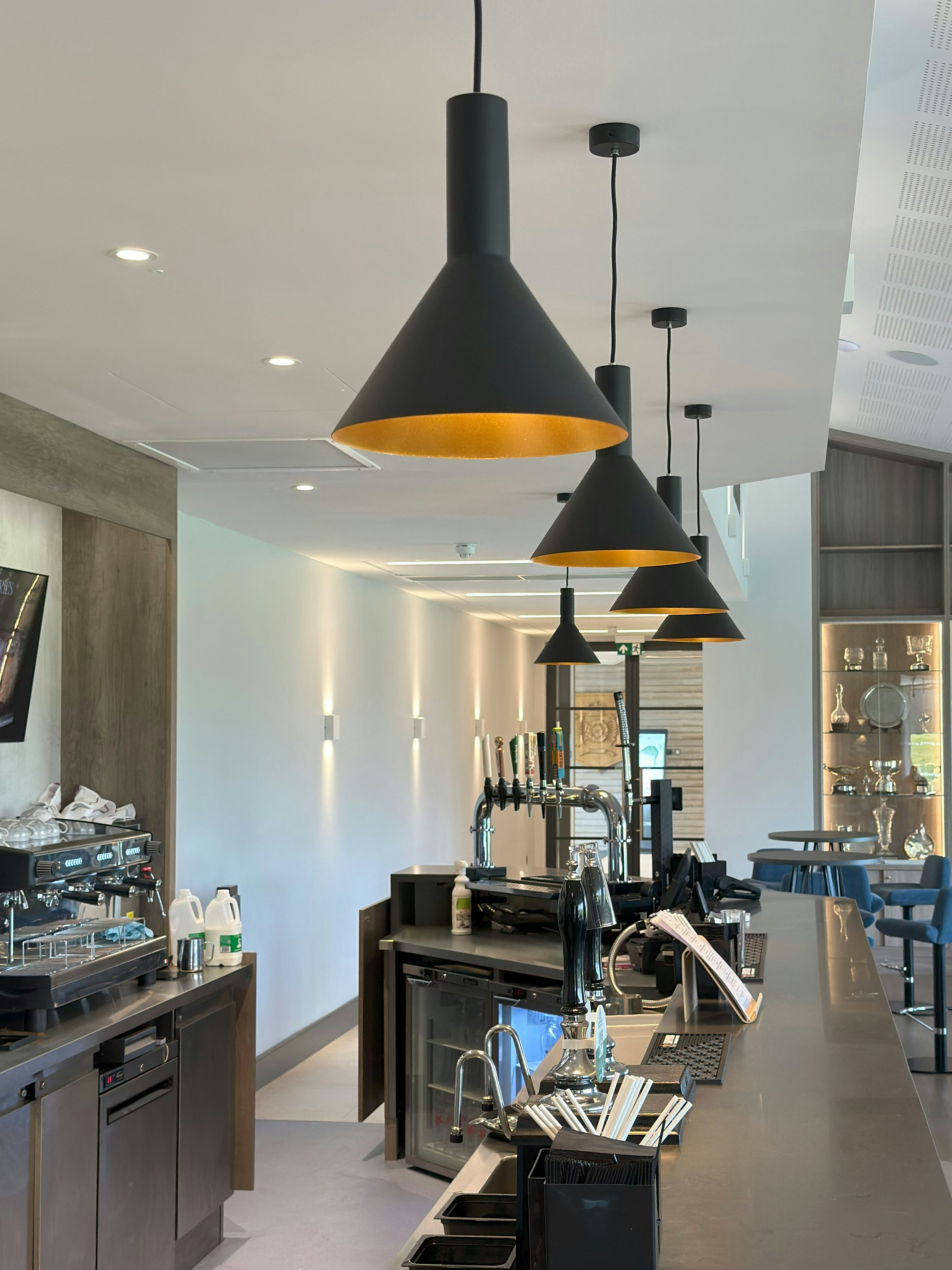 Black pendant lights hanging over a long bar counter in a modern cafe