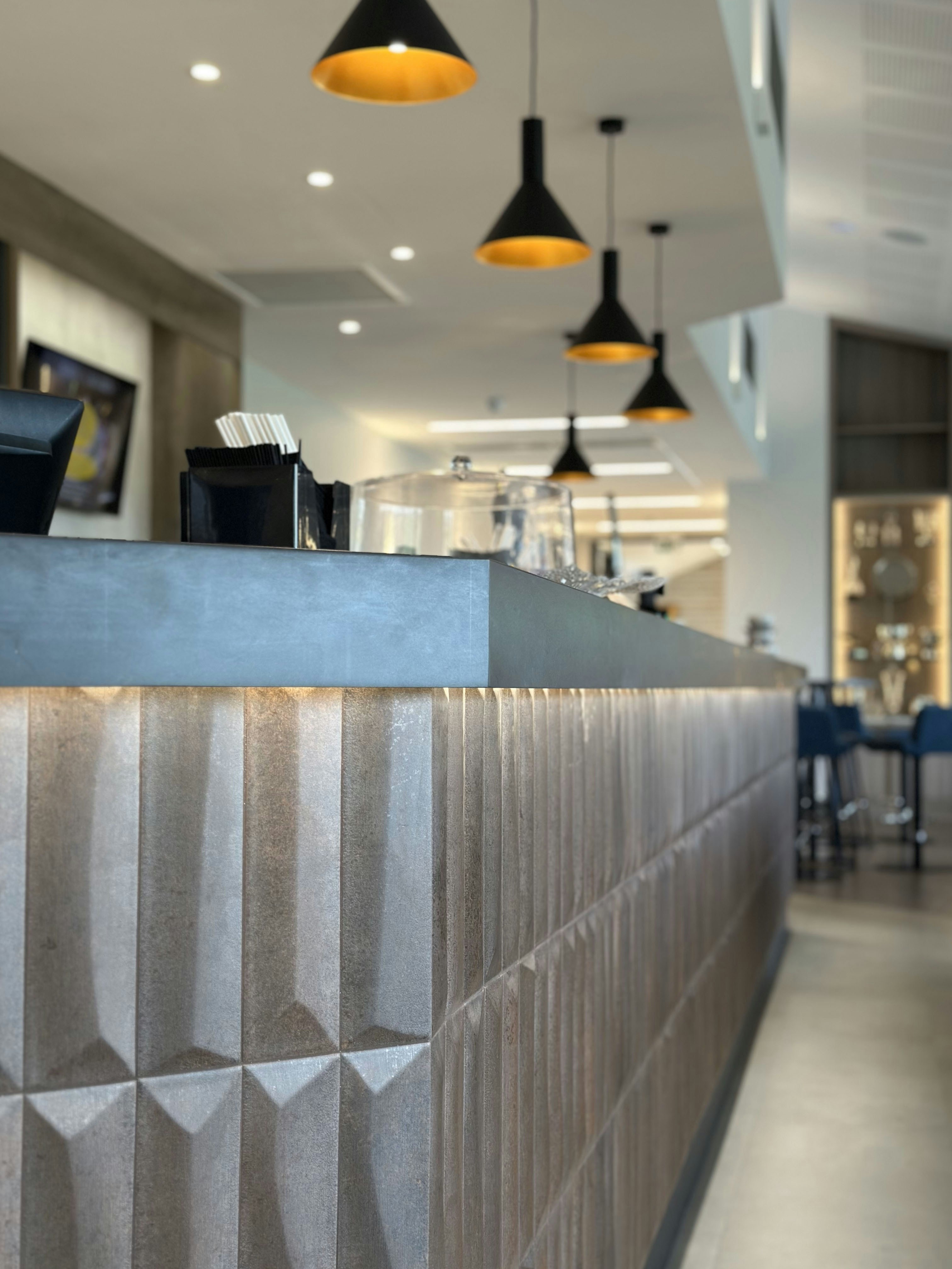 A modern cafe counter with textured grey panels and warm under-counter lighting