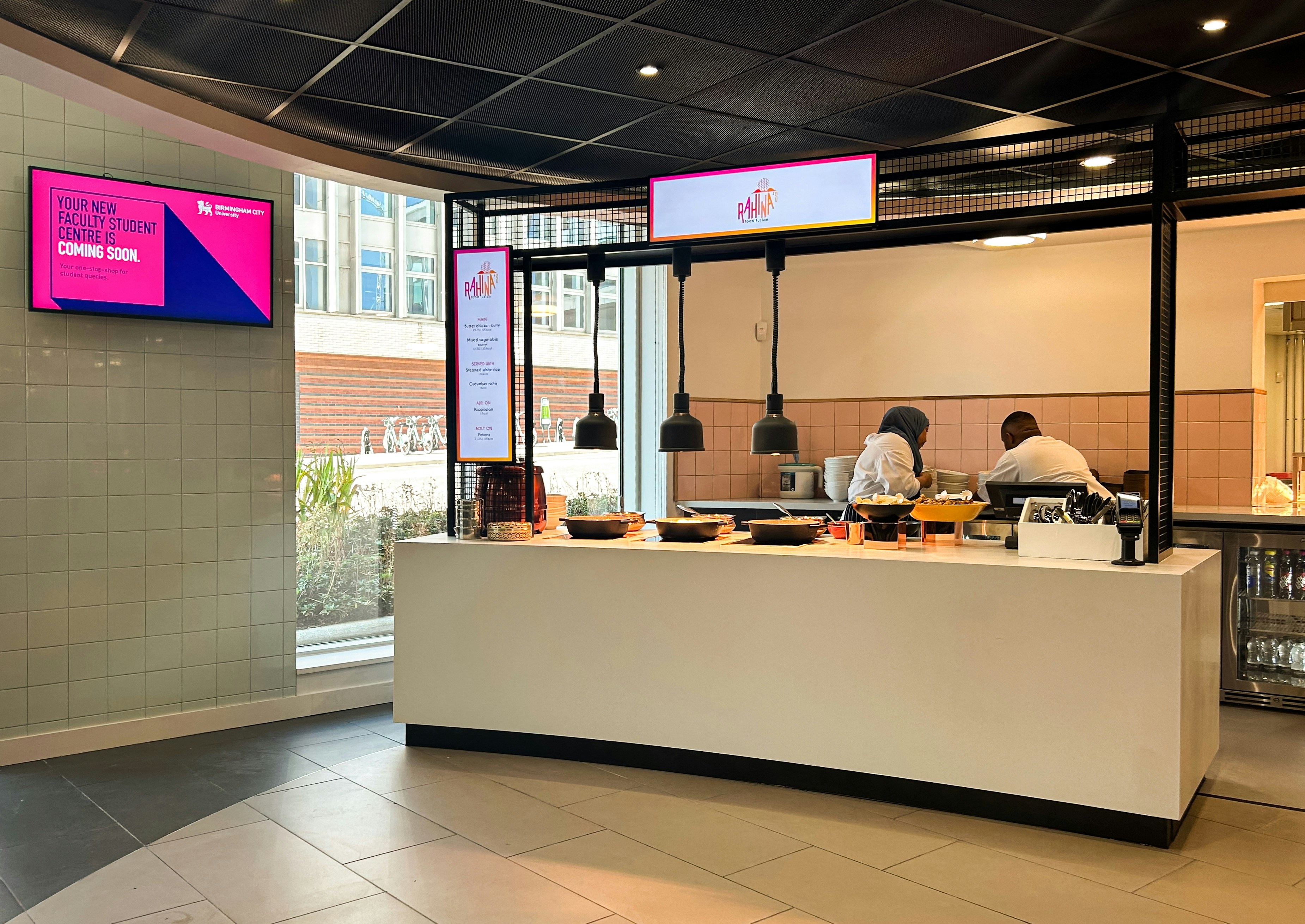 Two people working behind a food service counter in a bright modern cafeteria